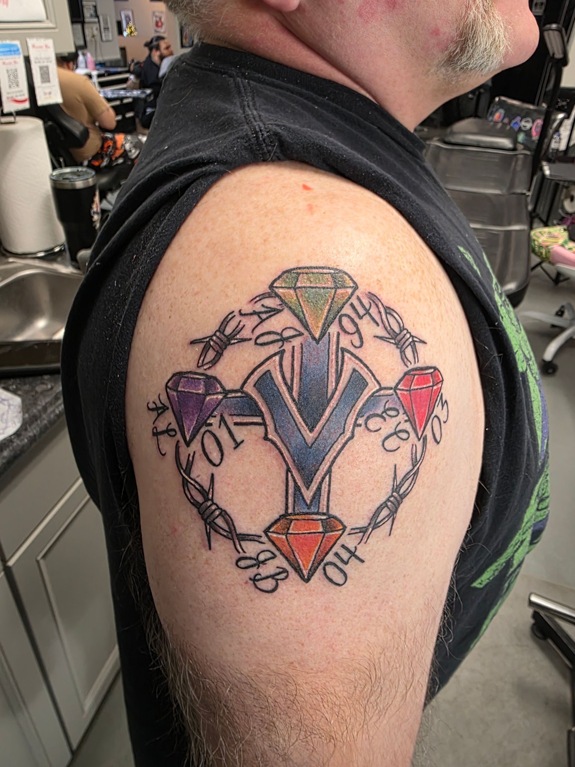 Tattoo of a cross with diamonds and barbed wire on a person's upper arm.