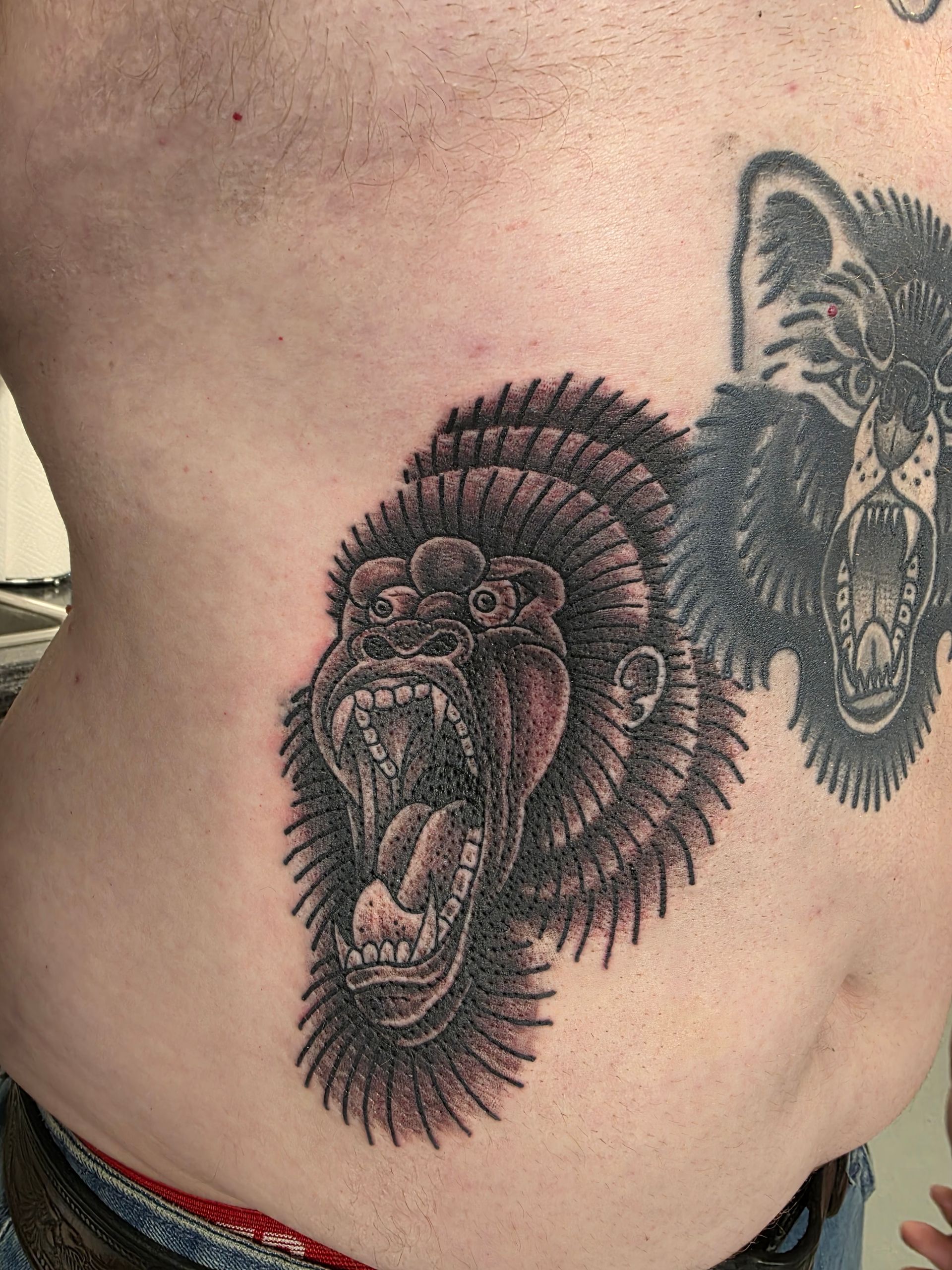Tattoo of an angry gorilla face with open mouth and a dark, detailed wolf head tattoo on chest.