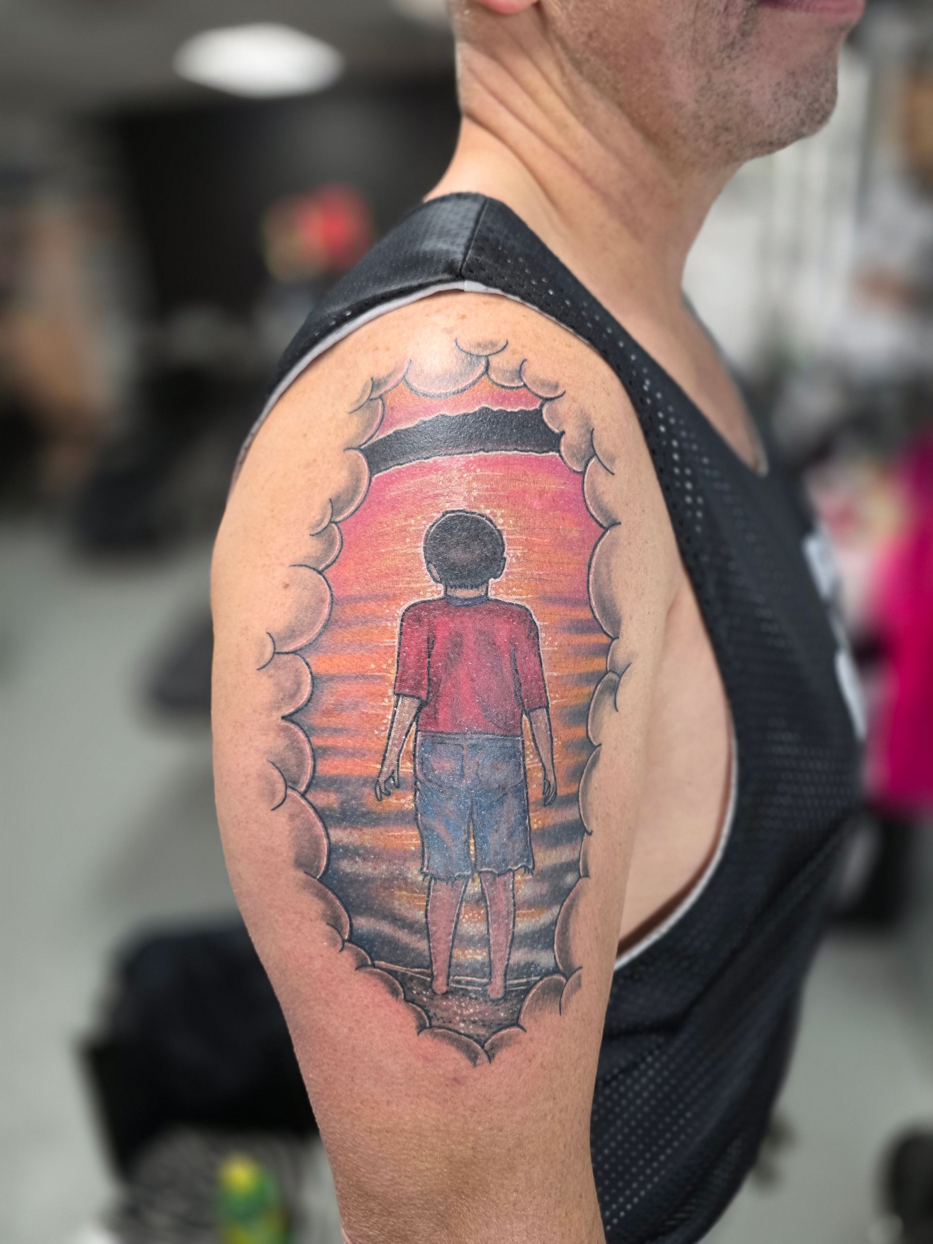 Tattoo on arm depicts a child looking at sunset through a torn skin effect.