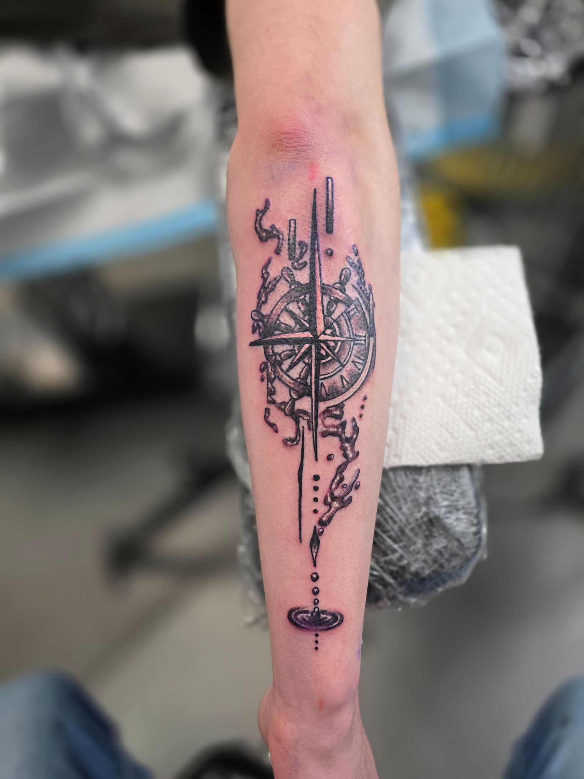 Tattoo of a compass-like design with abstract elements on a forearm.