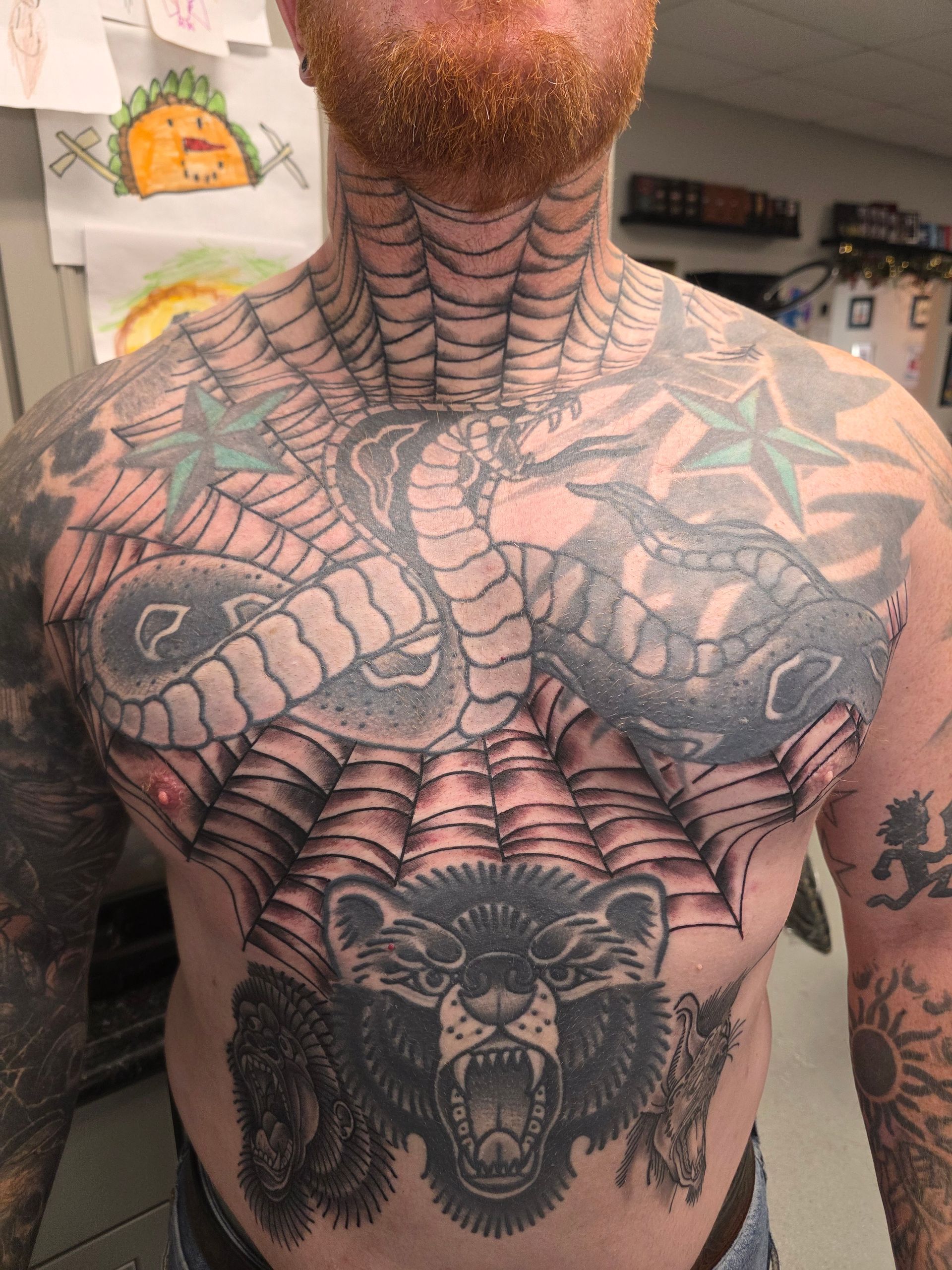 Man with extensive chest and neck tattoos: spiderwebs, bear, snake, and stars.