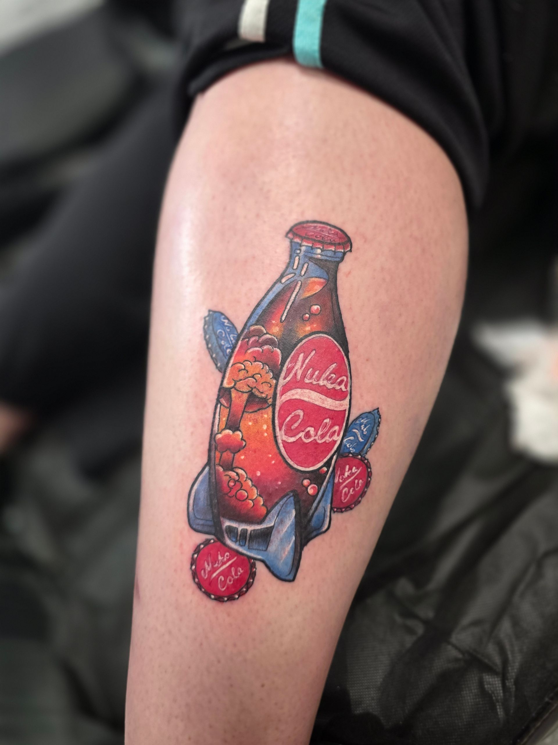 Tattoo of a Nuka-Cola bottle rocket on a leg, with blue fins, and red accents.