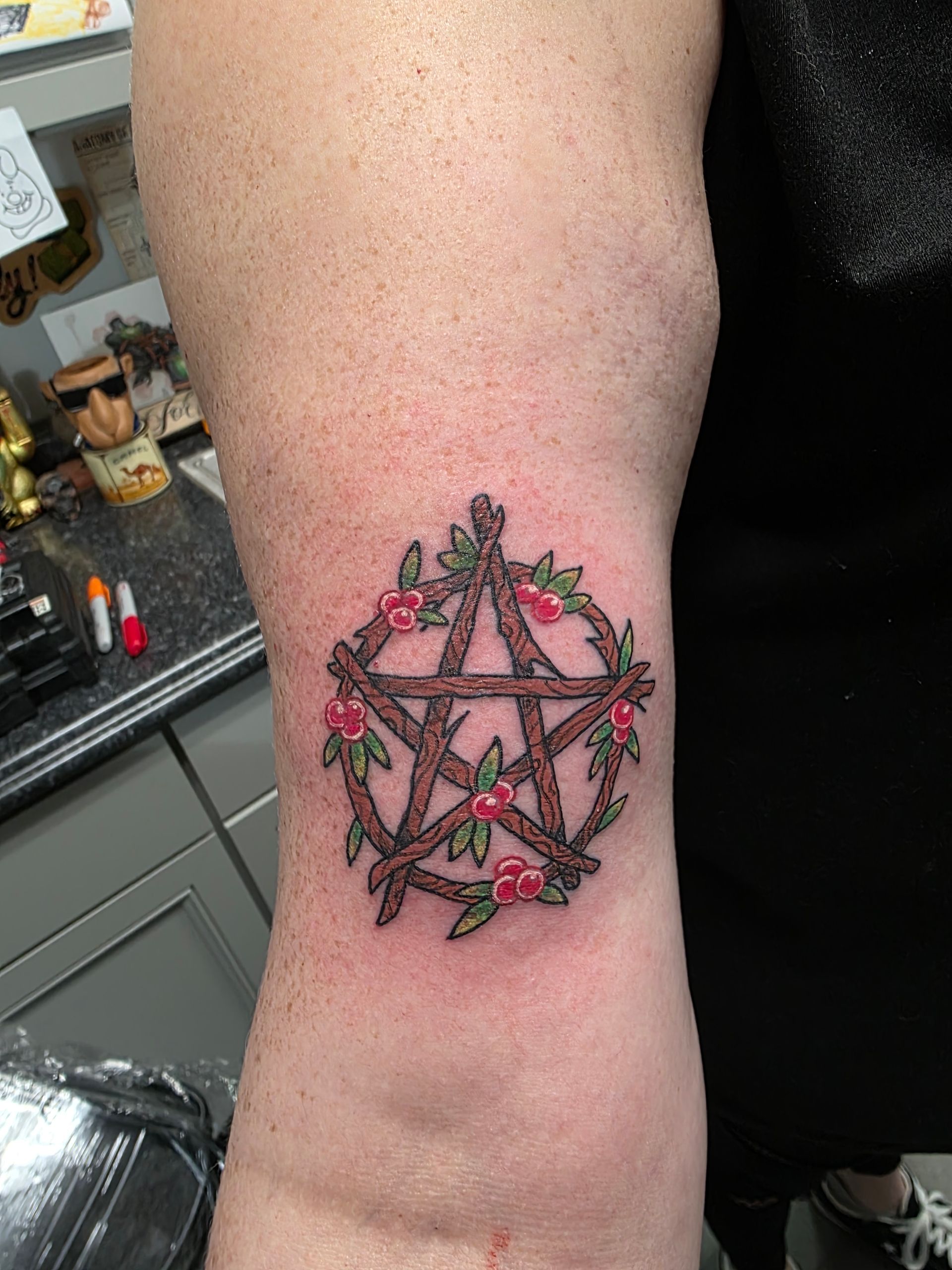 Tattoo of a wooden pentagram encircled by berries and foliage on a person's leg.