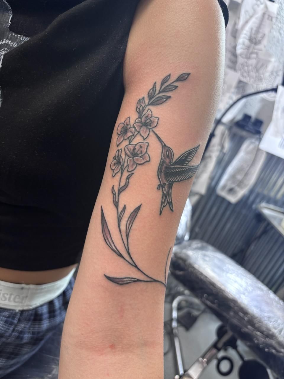 Tattoo of a hummingbird sipping nectar from a floral branch on a person's arm.