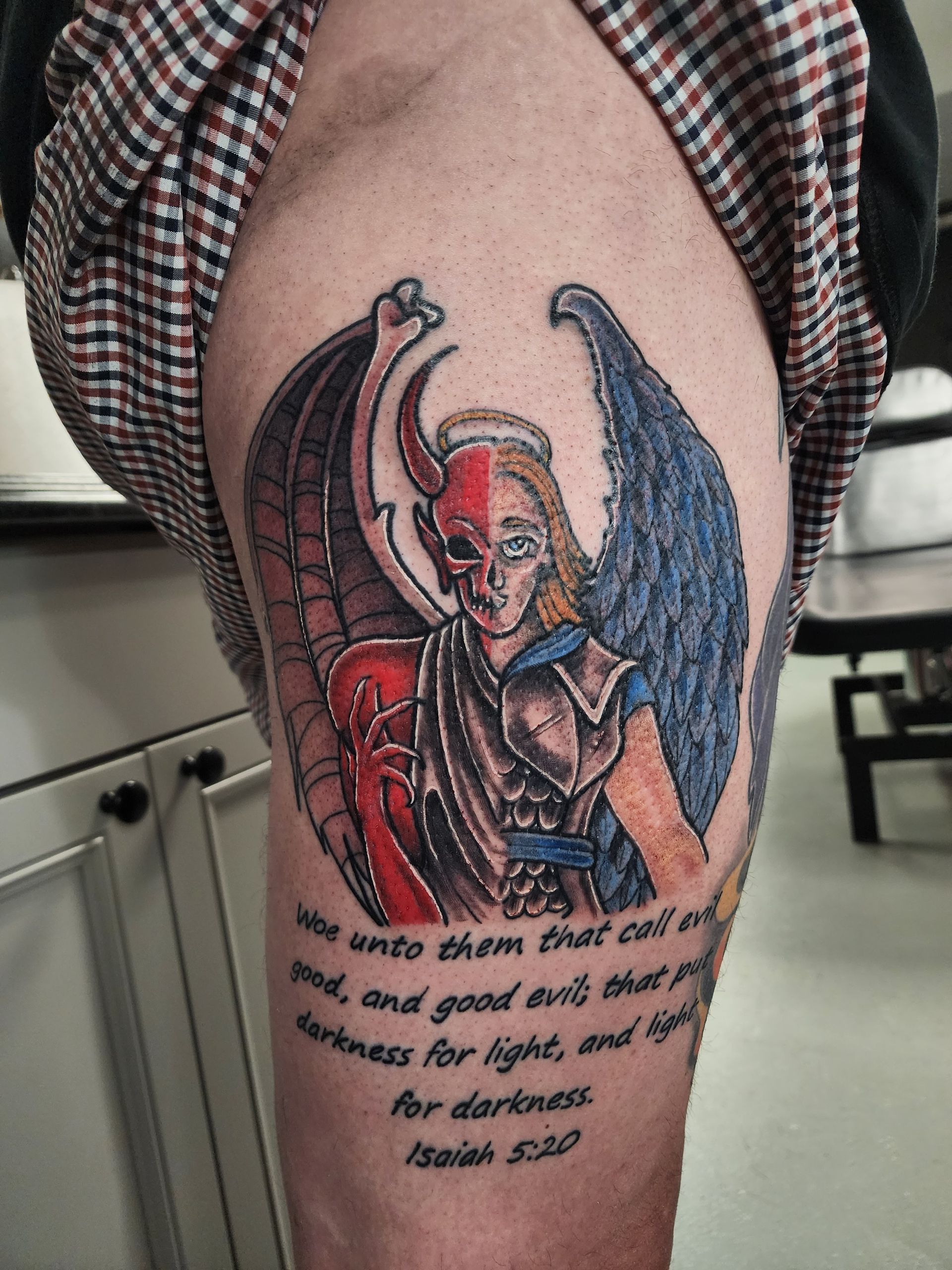 Tattoo of a half angel, half demon with wings. Quote from Isaiah 5:20 on the leg.