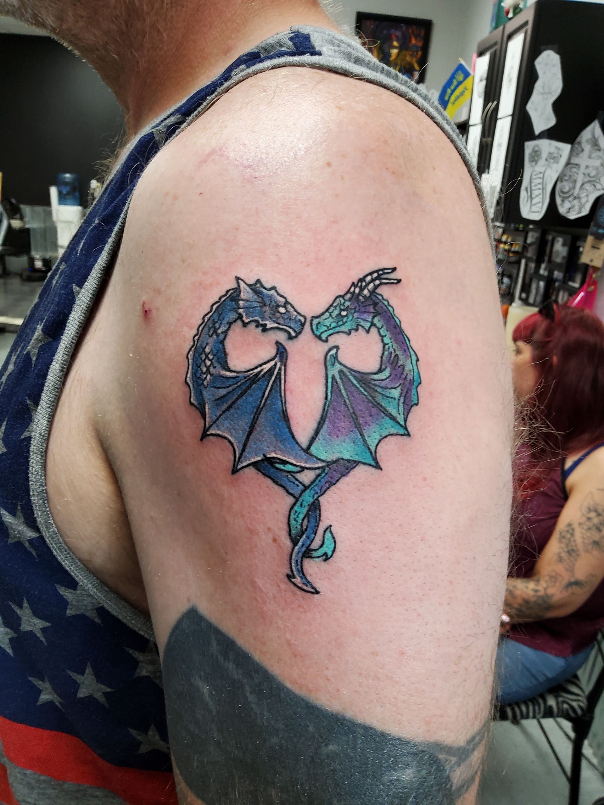 Tattoo of two blue dragons forming a heart shape on a person's upper arm.