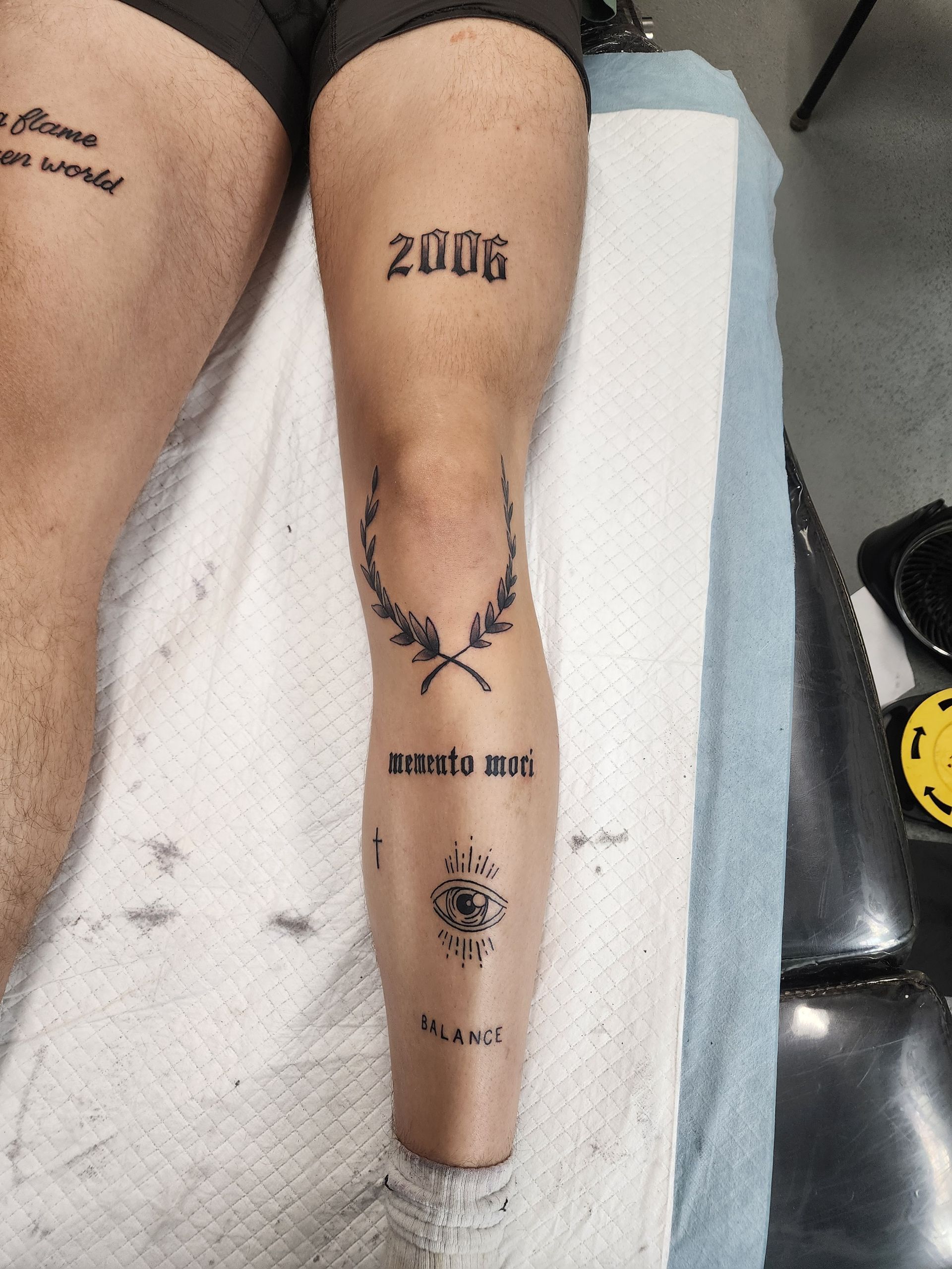 Leg with tattoos, including the year 2006, a laurel wreath, and text. The leg is resting on a white towel.