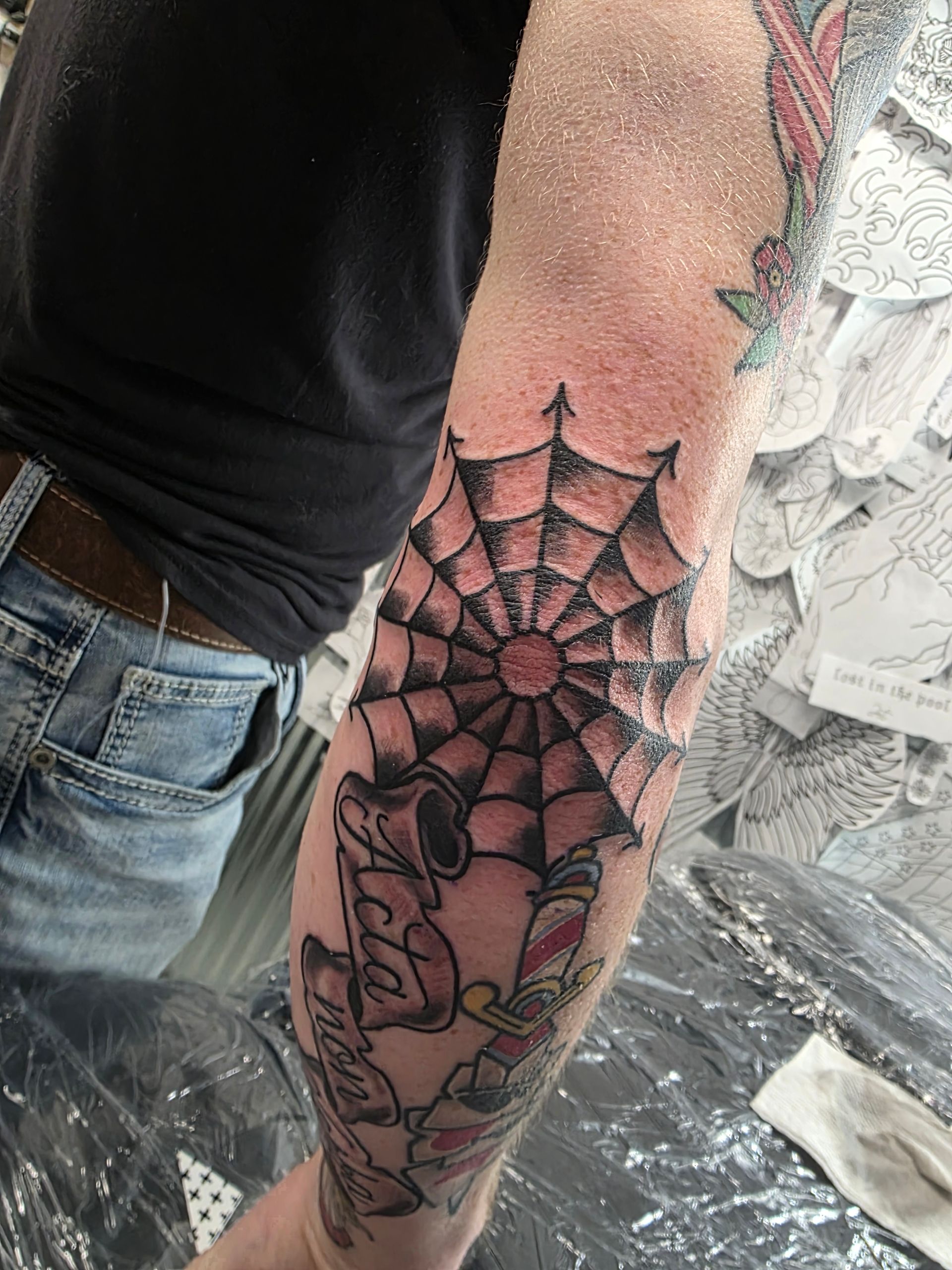 Arm with tattoo featuring a spider web and cartoon characters in black ink.