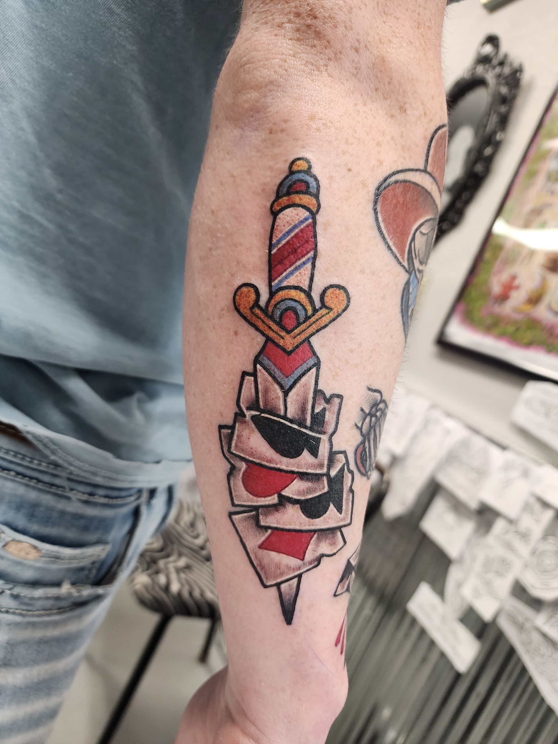 Tattoo of a dagger piercing playing cards on a person's forearm. Red, blue, gold, and black colors.