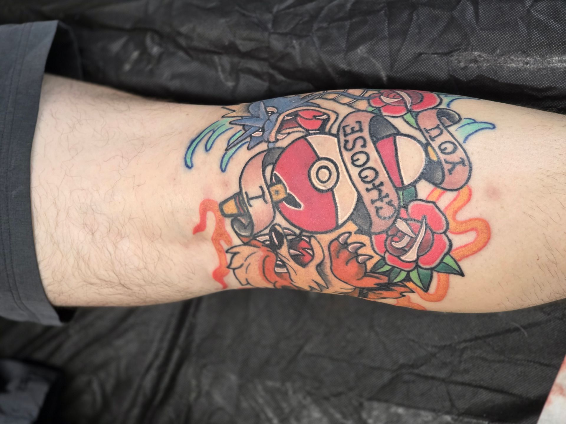 Tattoo of a Pokéball, roses, and a Charmander on a person's knee, with the words 