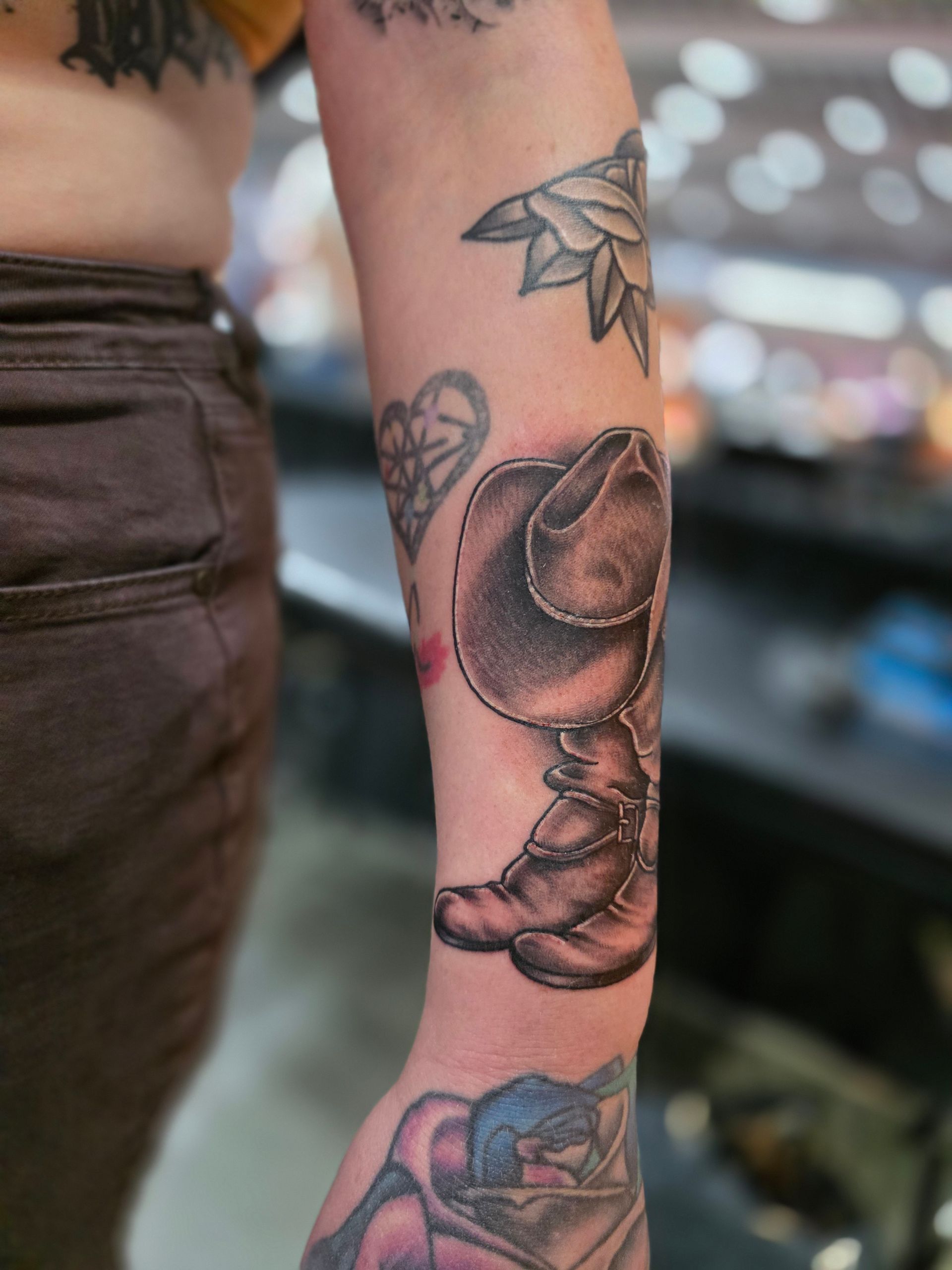 Arm tattoo of a cartoon cowboy with hat and boots. Other tattoos are also visible on the arm.