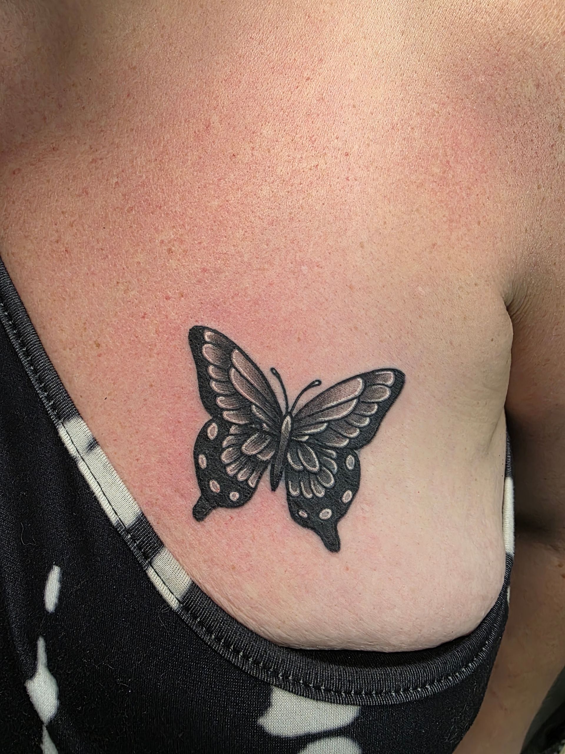 Butterfly tattoo on a person's chest, black and gray shading, textured wing details.