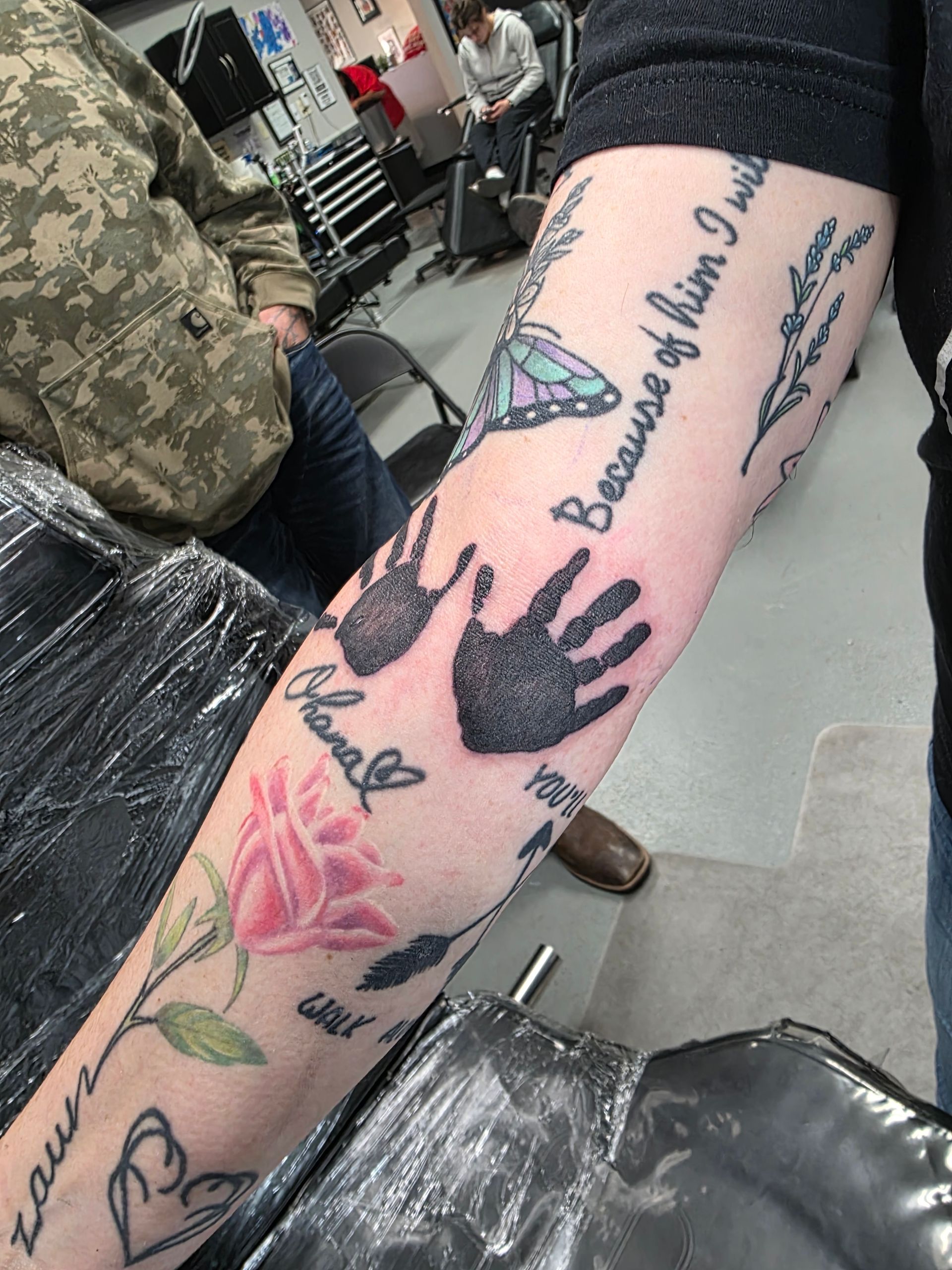 Arm tattoo featuring handprints, rose, butterfly, and text.