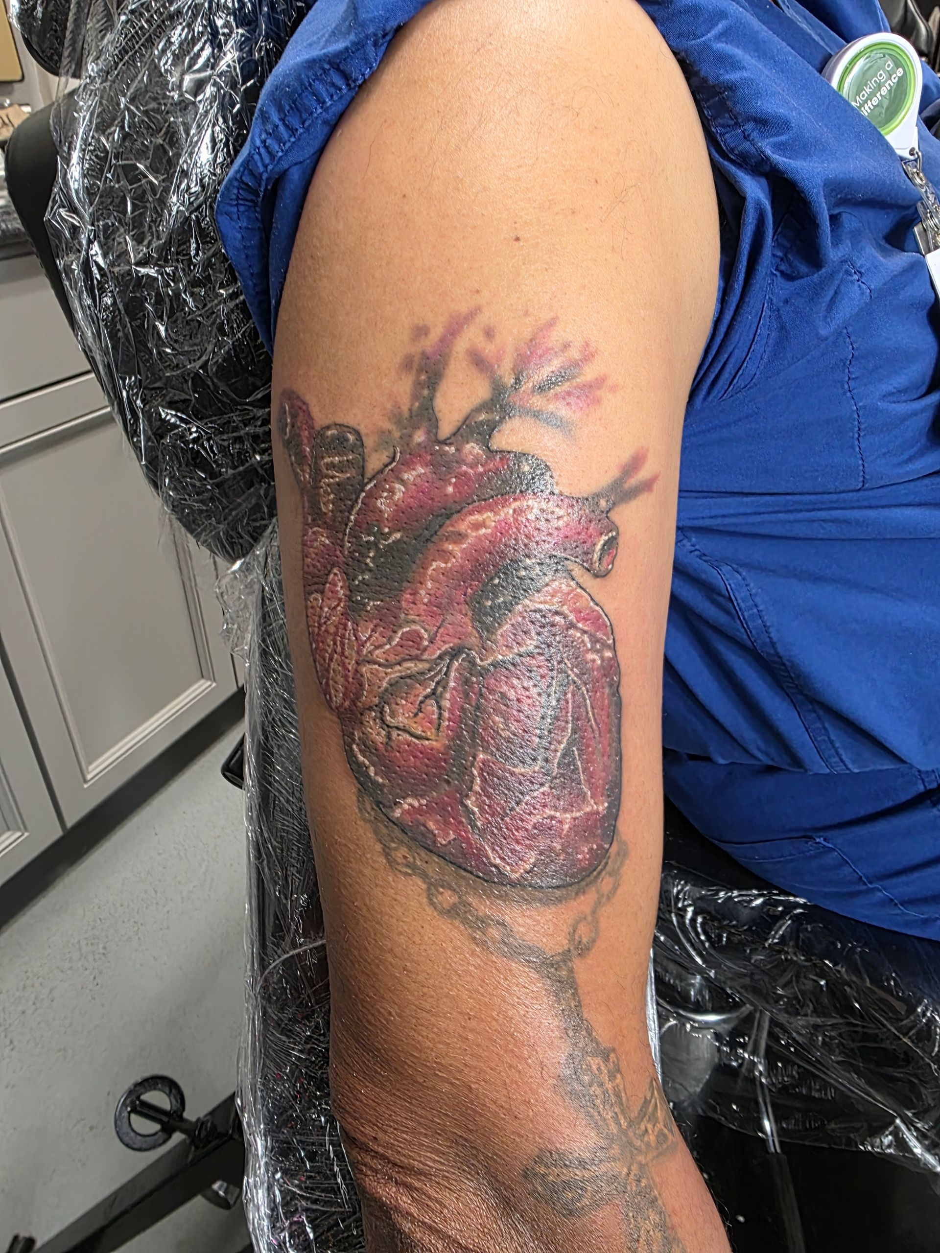 Tattoo of a human heart on a person's upper arm. The heart is red with visible details and black shading.