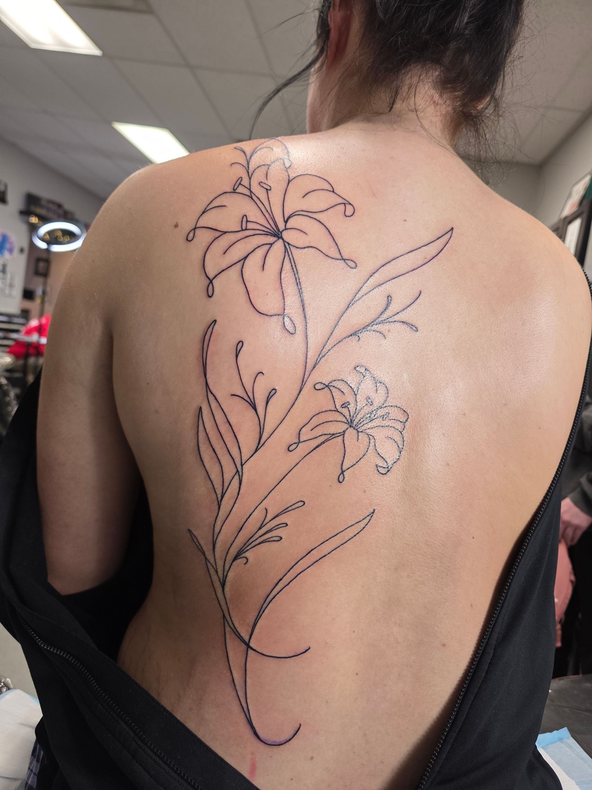 Back tattoo of two lilies on a woman's back, black outline.