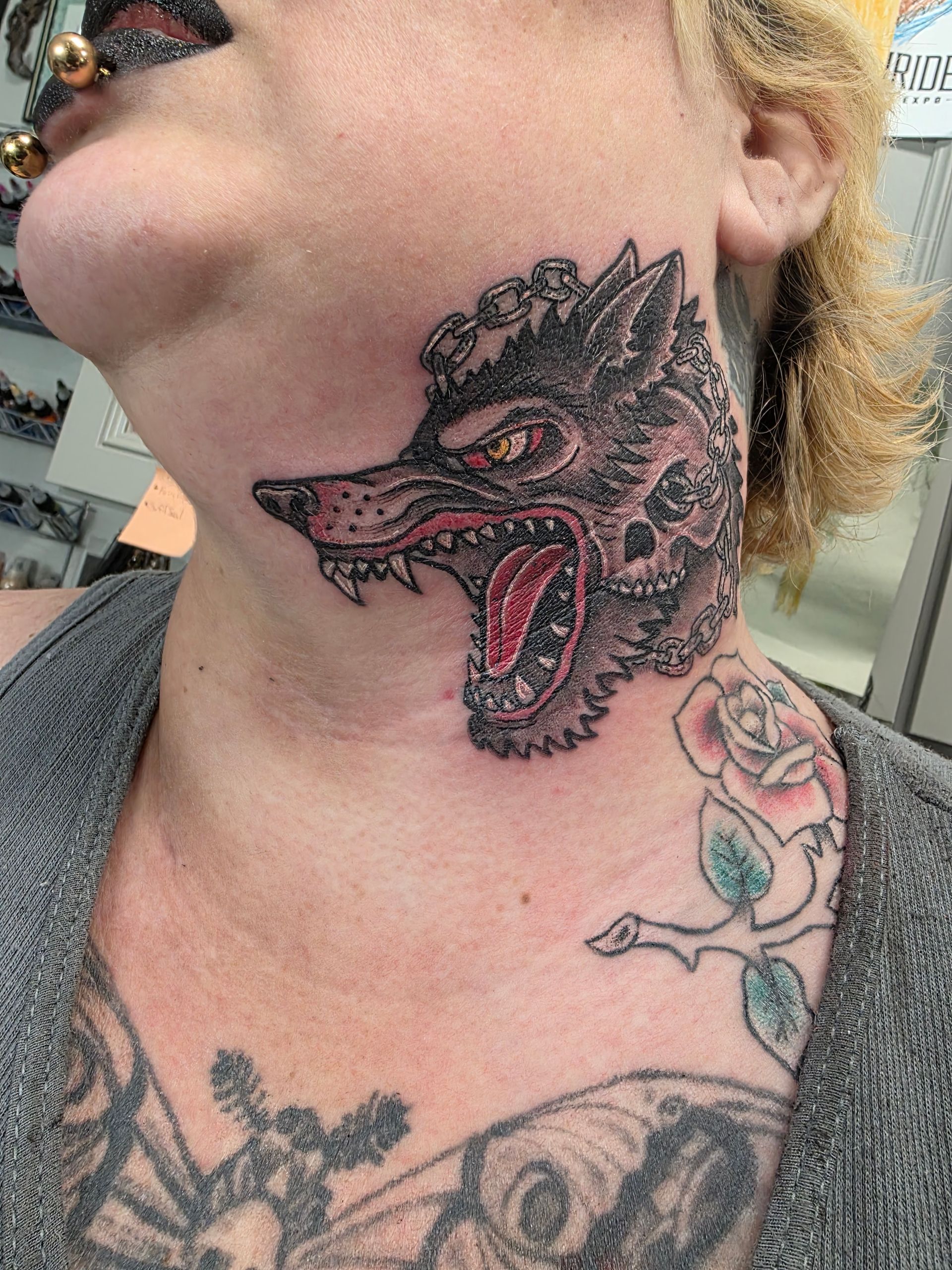 Neck tattoo: snarling wolf, red tongue, rose. The person has ear and nose piercings.