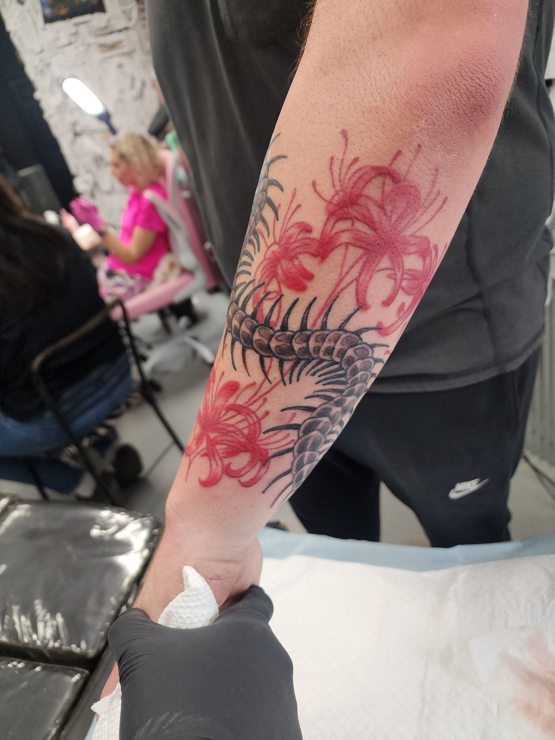 Tattoo of red flowers and dark plant design on an arm in a tattoo studio.