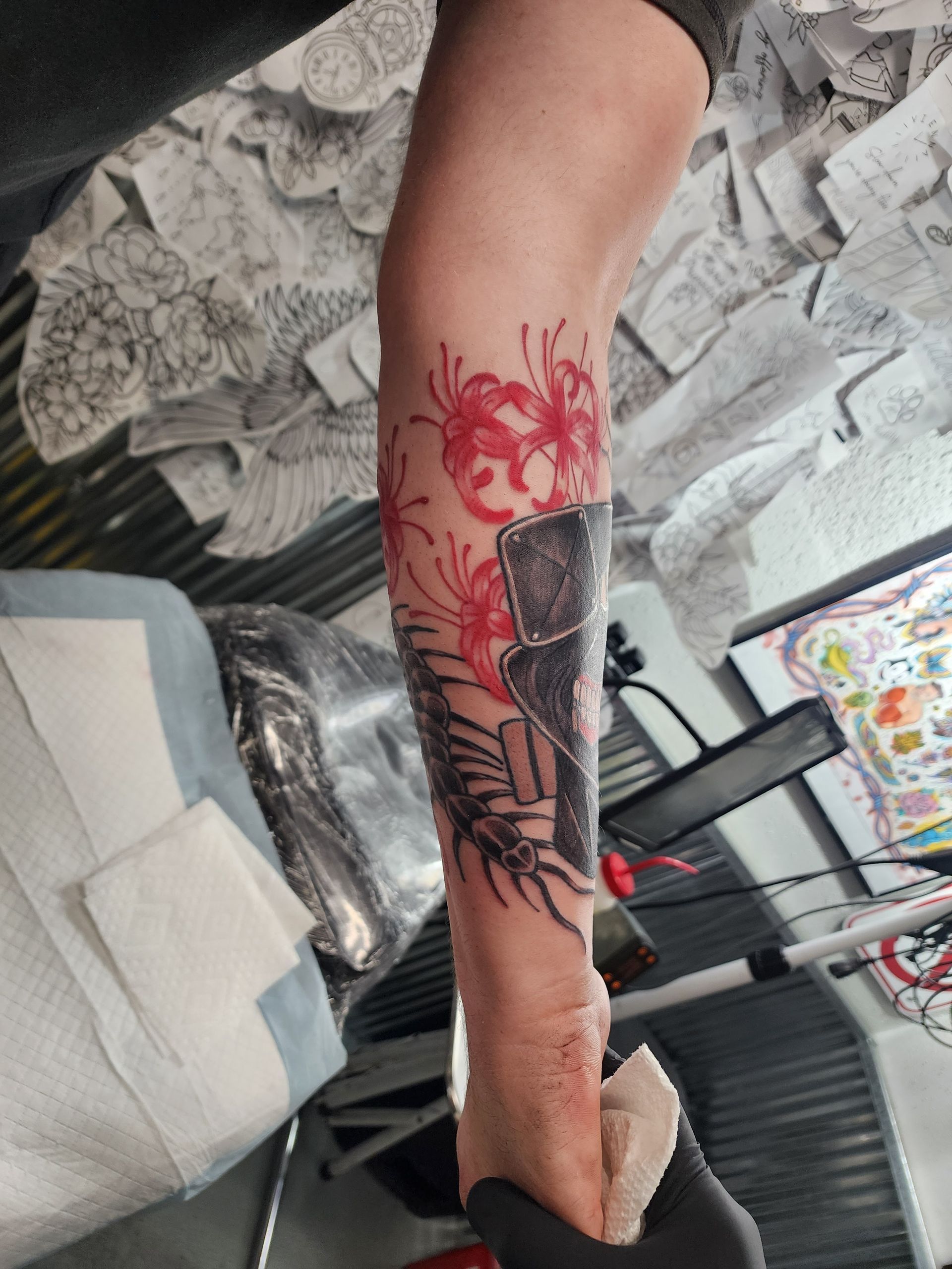 Arm with a red and black tattoo of flowers and a rectangular shape, possibly a building.