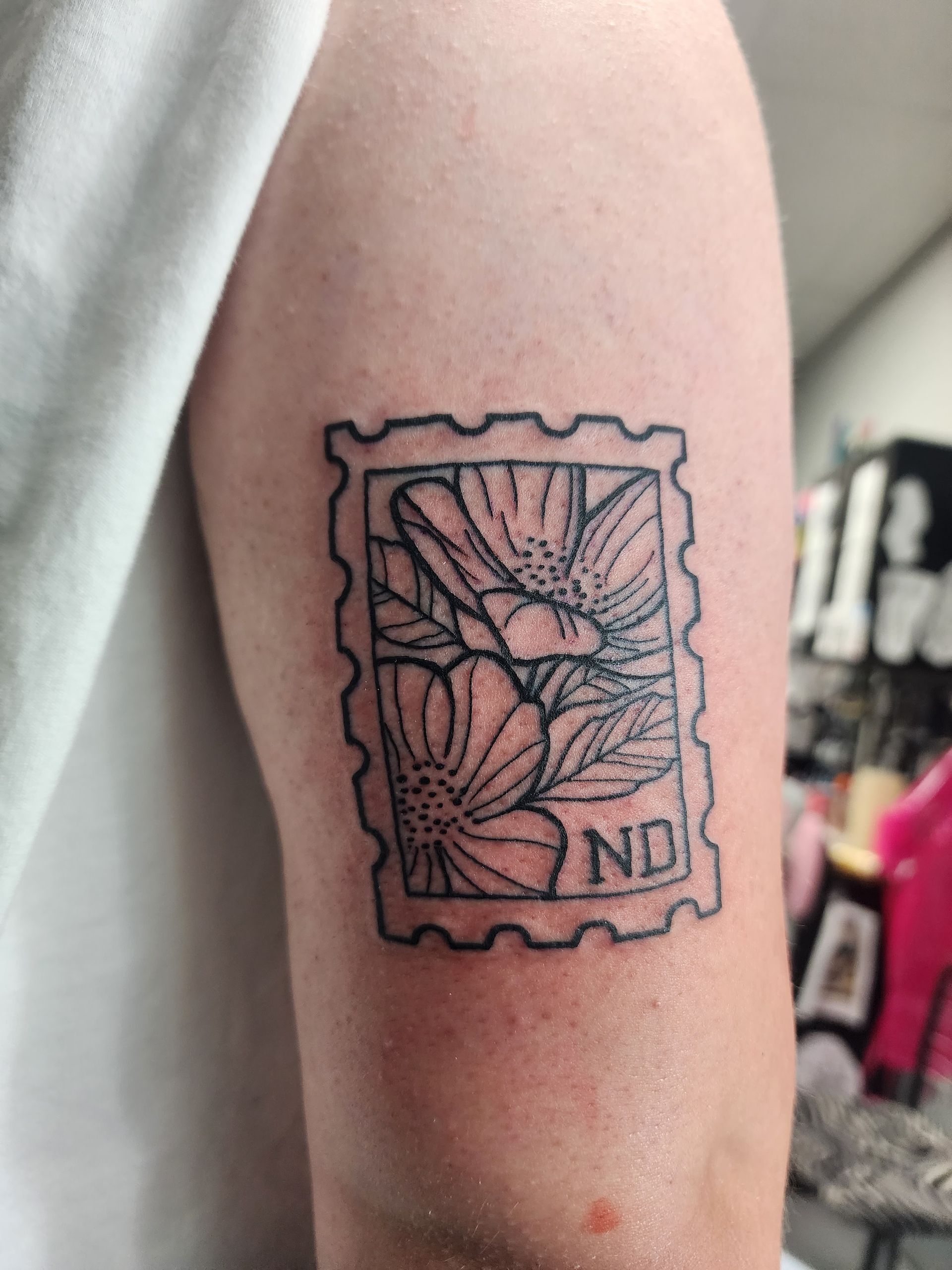 Tattoo of a floral design inside a postage stamp outline on a person's arm. 