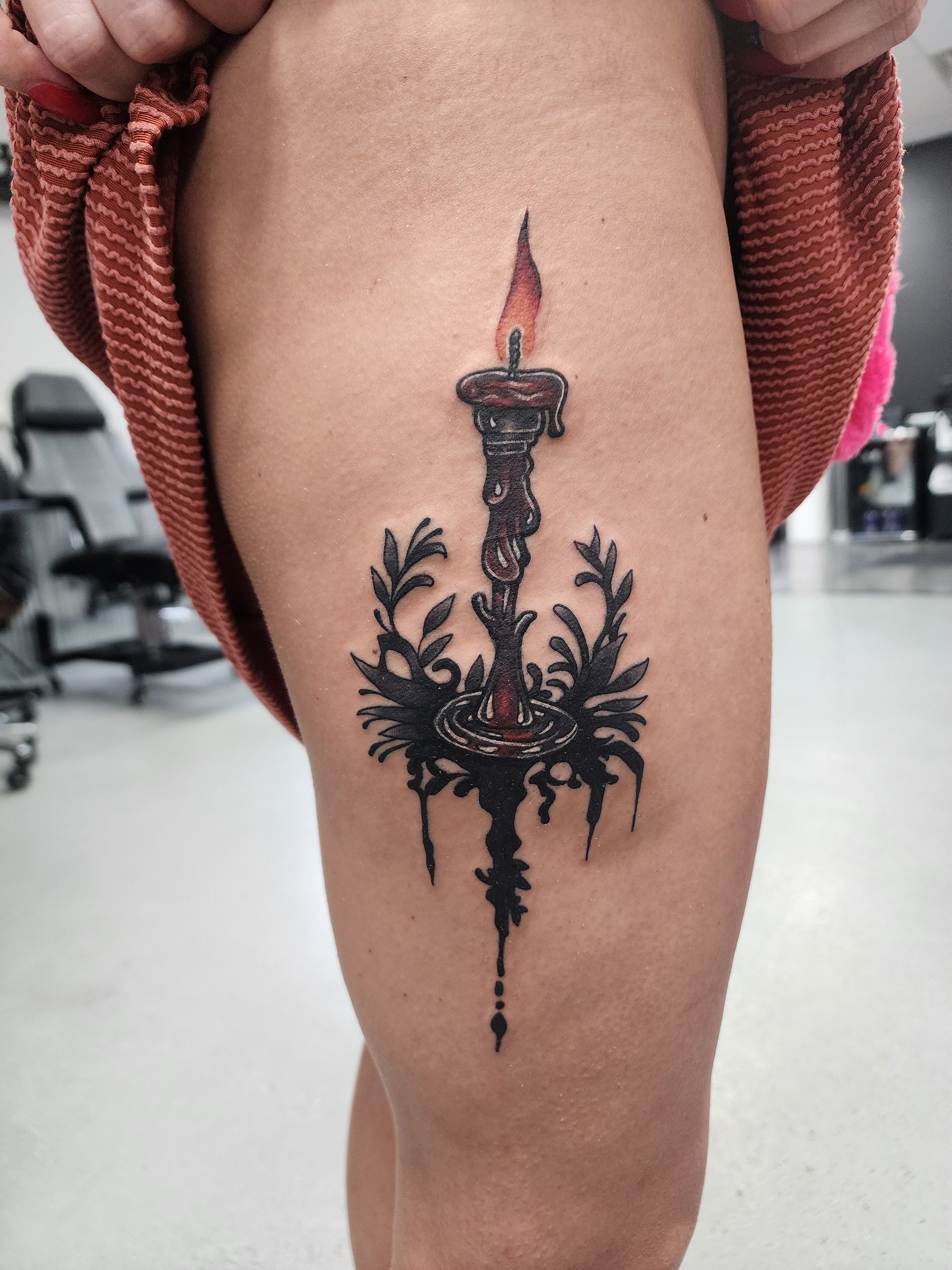Tattoo of ornate candle with dripping wax and foliage on a person's thigh.