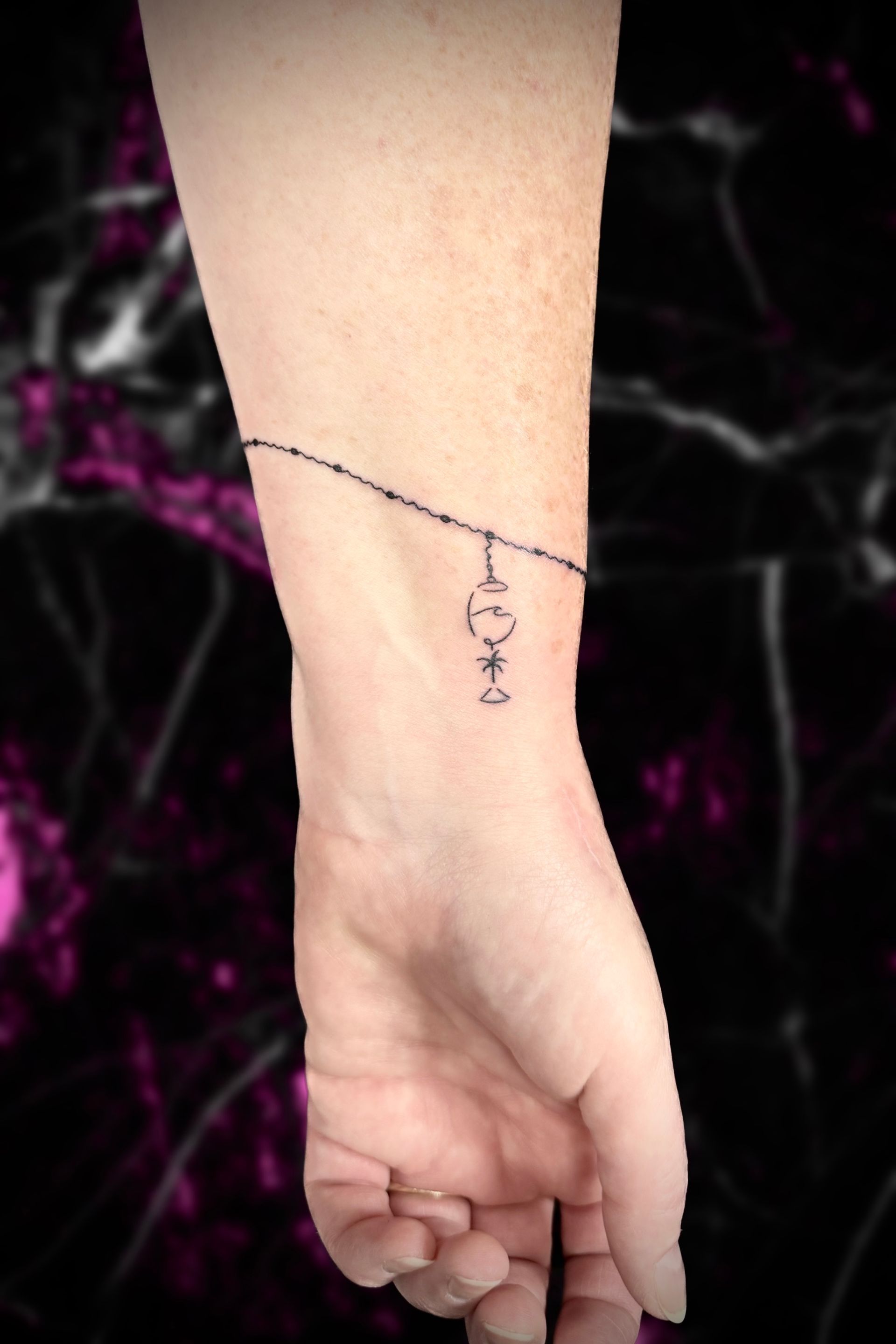 Wrist with tattoo resembling a delicate bracelet and pendant.