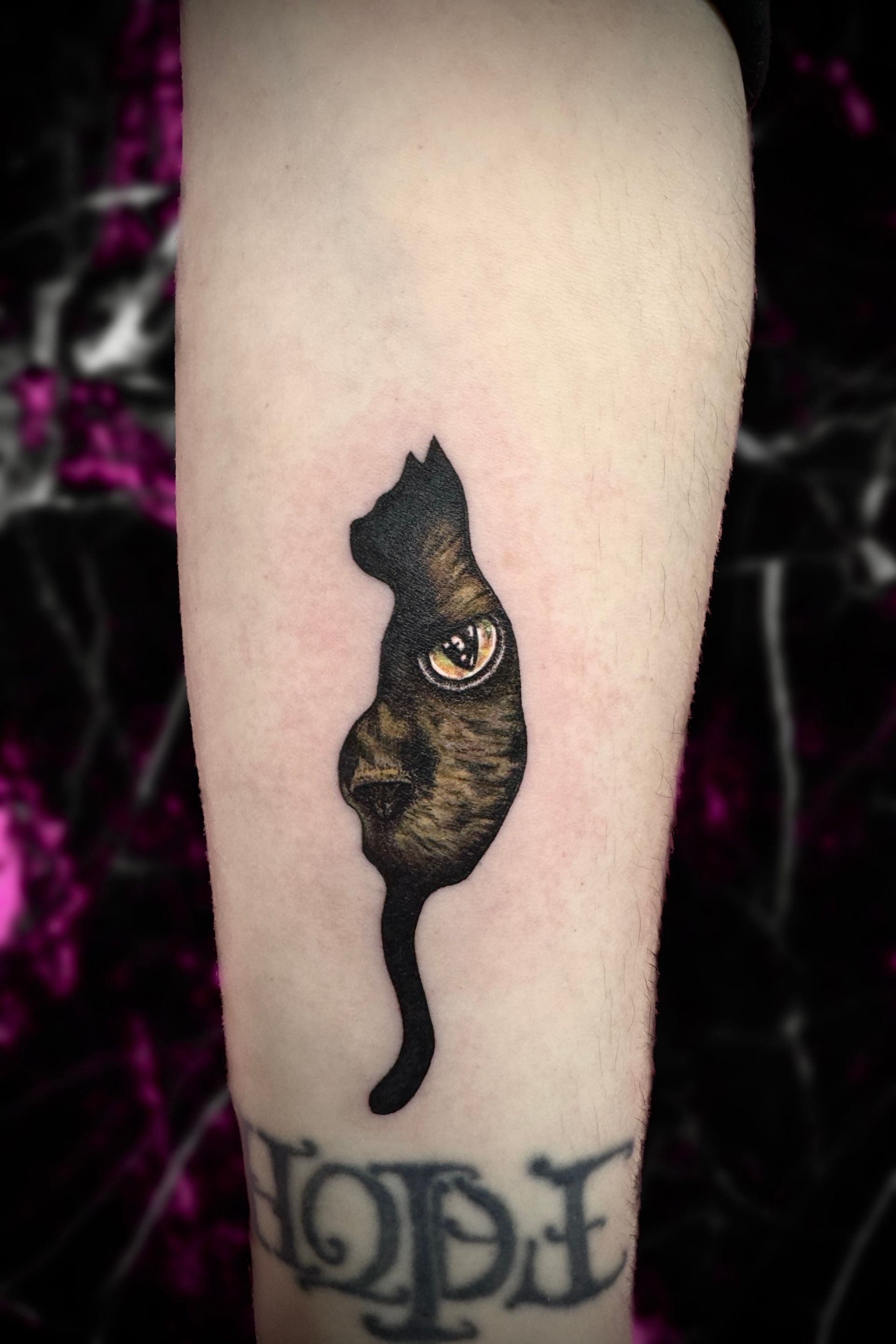 Tattoo of a black cat silhouette with an eye design, on a person's arm.