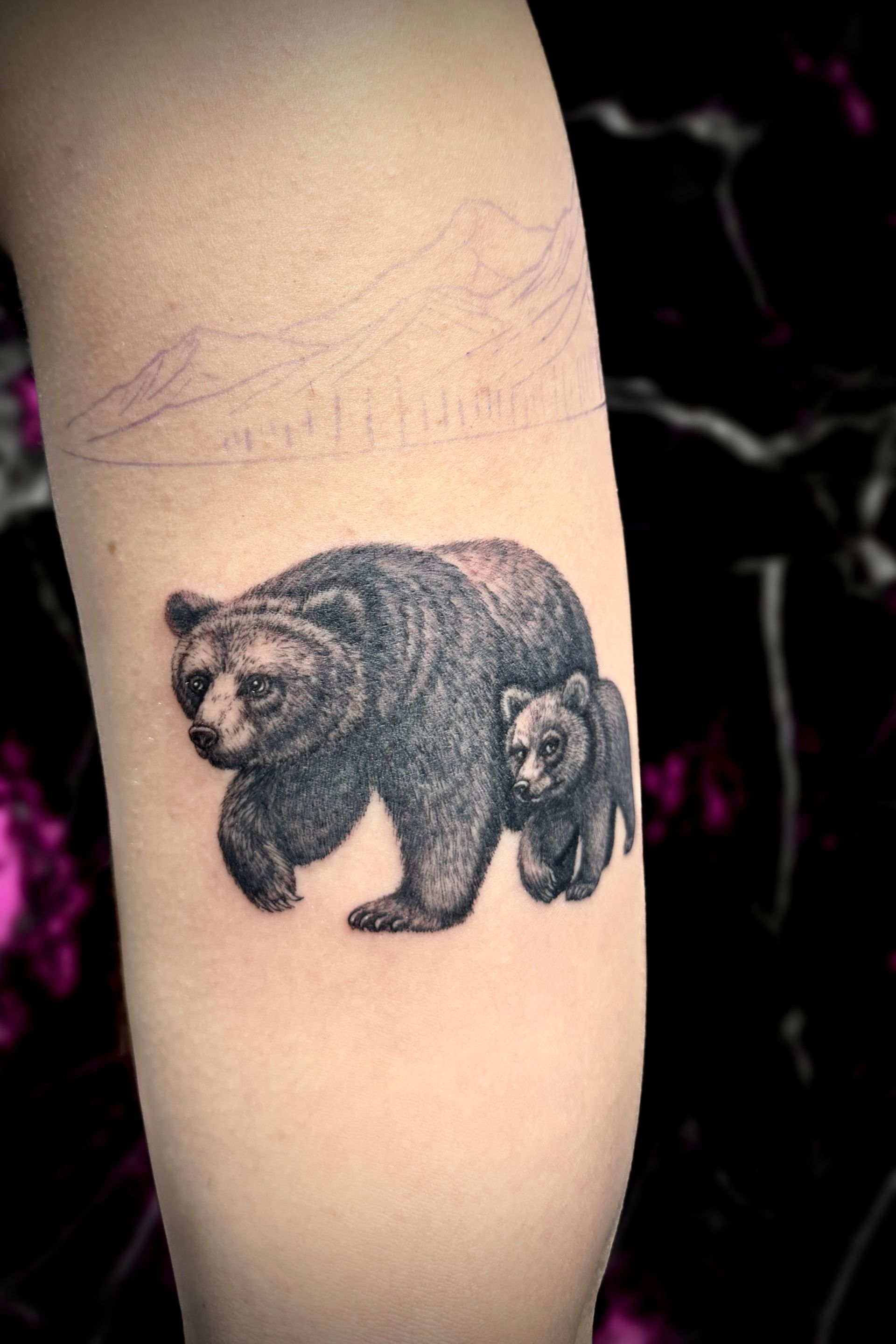 Tattoo of a large bear walking with a smaller cub. Black and gray shading. On an arm.