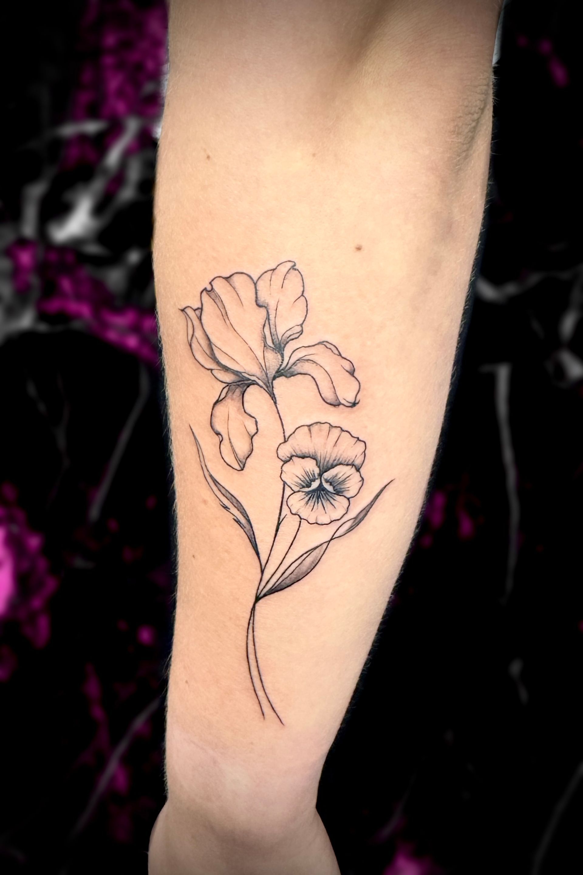 Line art tattoo of an iris and pansy on a person's forearm.