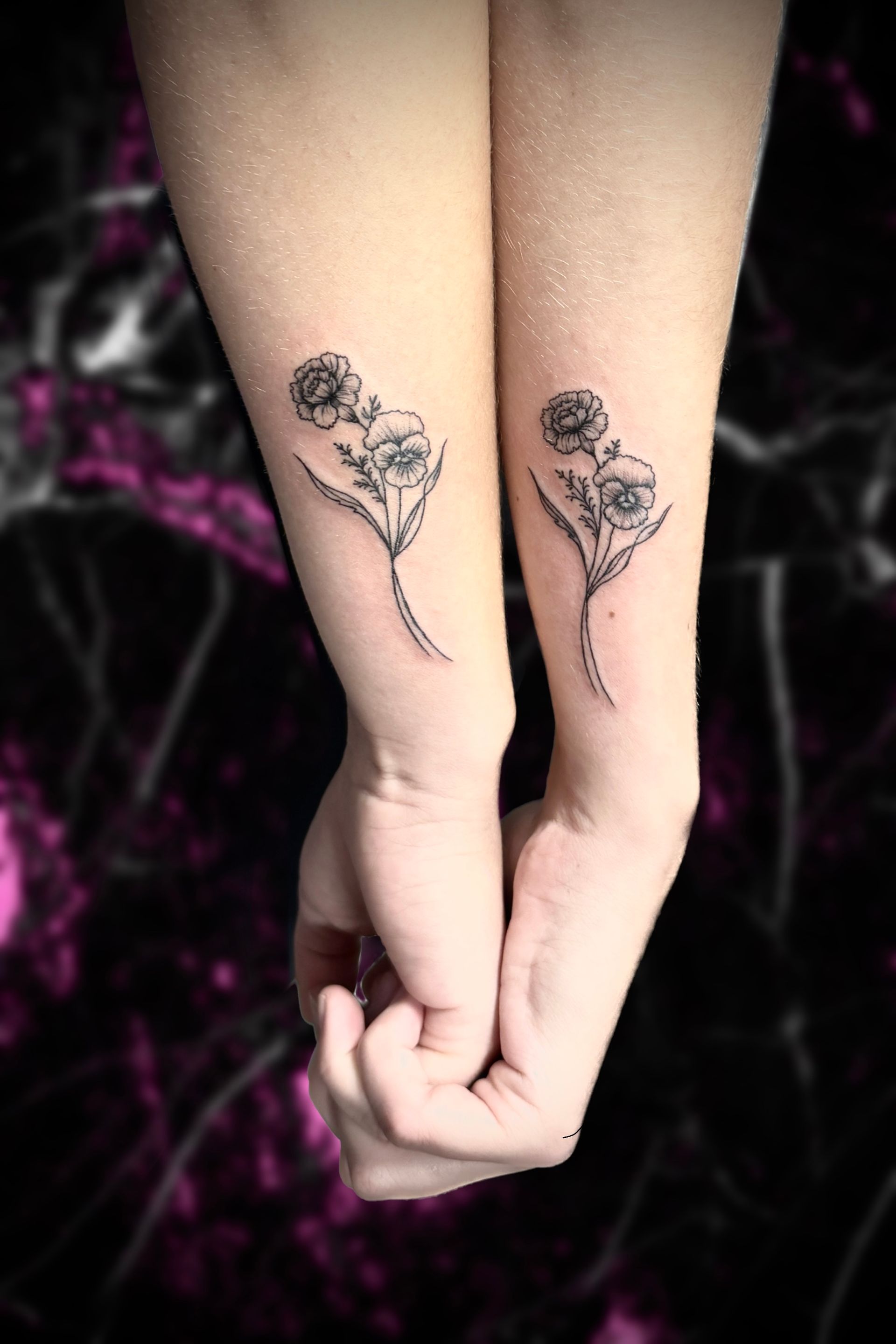 Matching floral tattoos on two forearms, held together. Black and white, delicate line art.