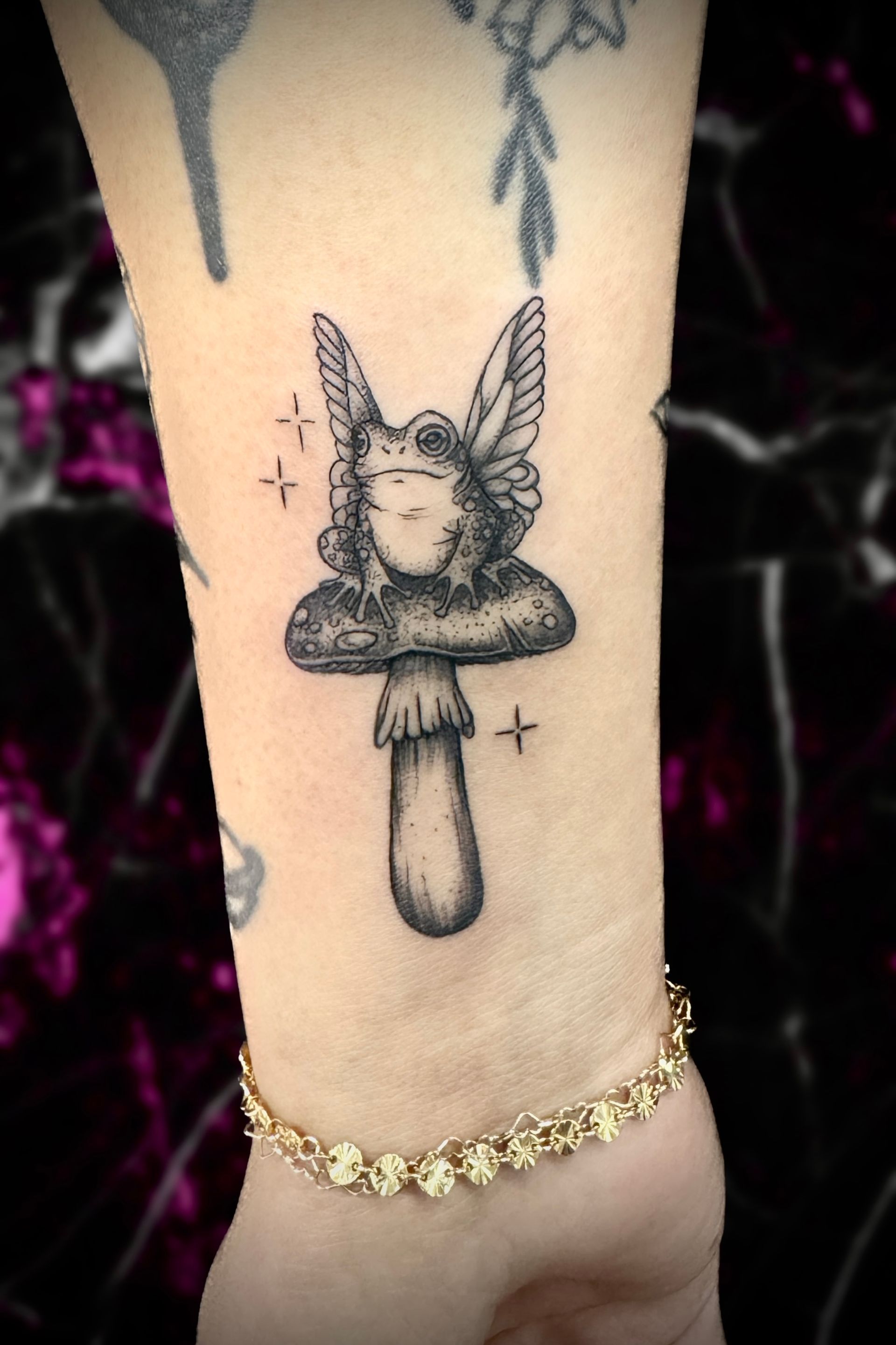 Black and white tattoo of a fairy like figure on a mushroom. Stars and a bracelet are also present.