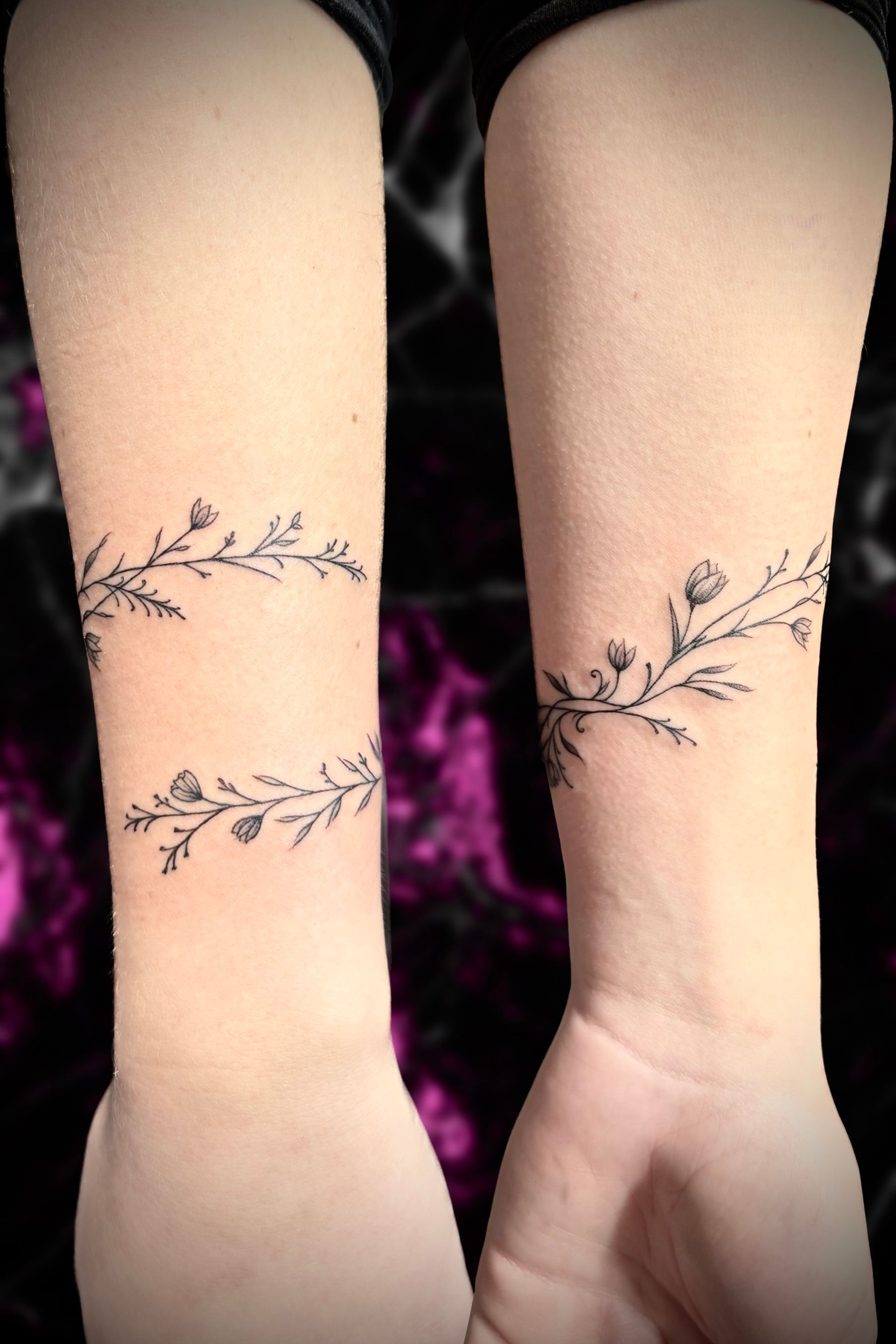Two wrists with delicate, black vine tattoos, one set of vines below the other.