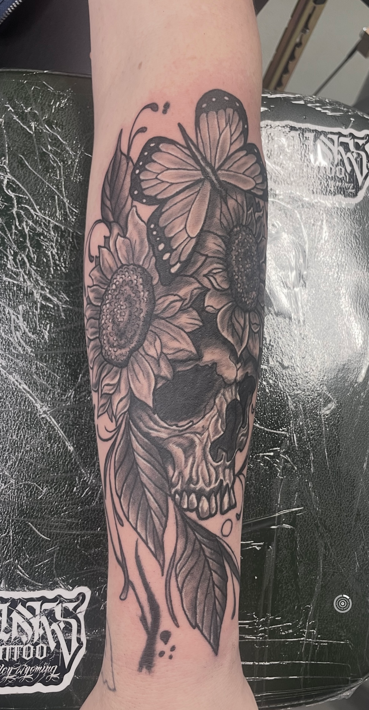 A black and white tattoo of a skull with flowers and butterflies