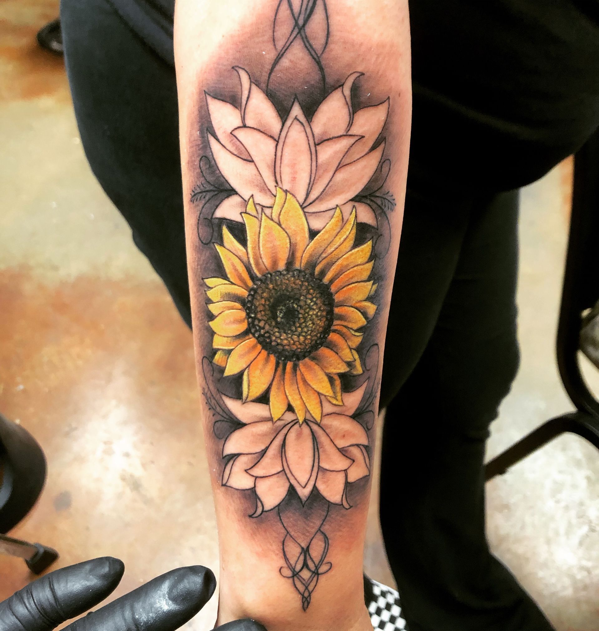 Tattoo of a yellow sunflower between two white lotus flowers, on a person's arm.