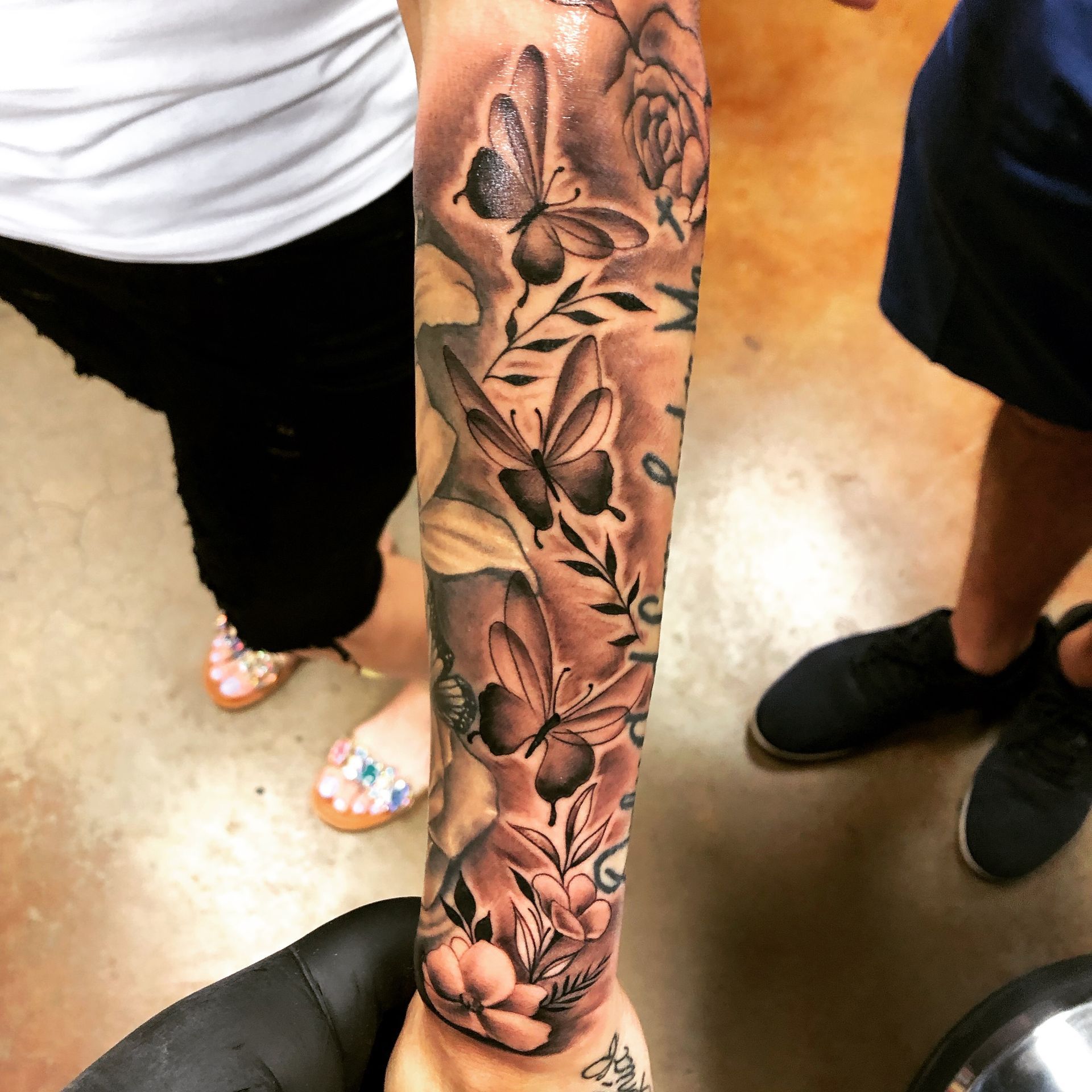 Arm tattoo with butterflies, leaves, flowers; black and white shading on skin.