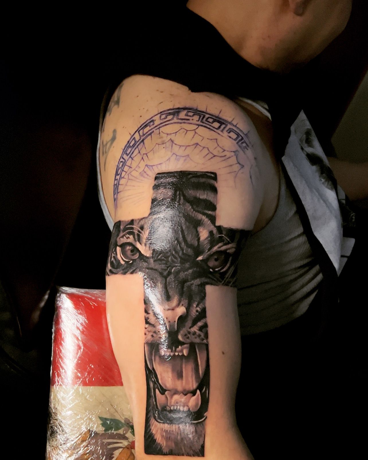 Tattoo of a tiger's face forming a cross on arm, with a partial circular design above.