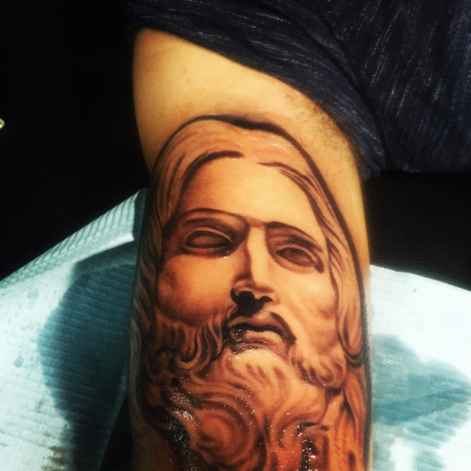 Arm tattoo of a bearded man's face, shaded in brown and black, with closed eyes.