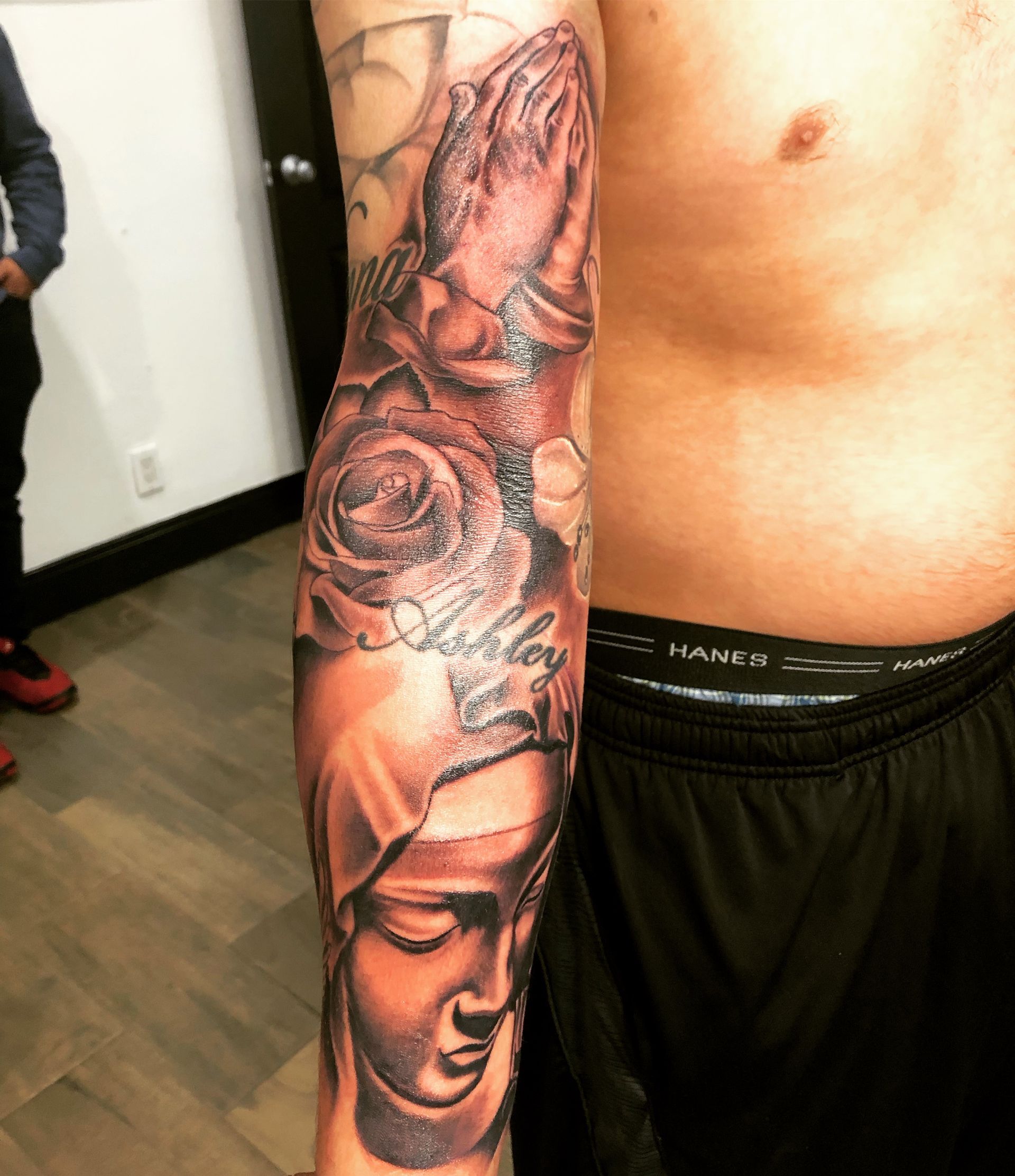 Tattoo sleeve: praying hands, roses, and a Virgin Mary portrait on a man's arm.