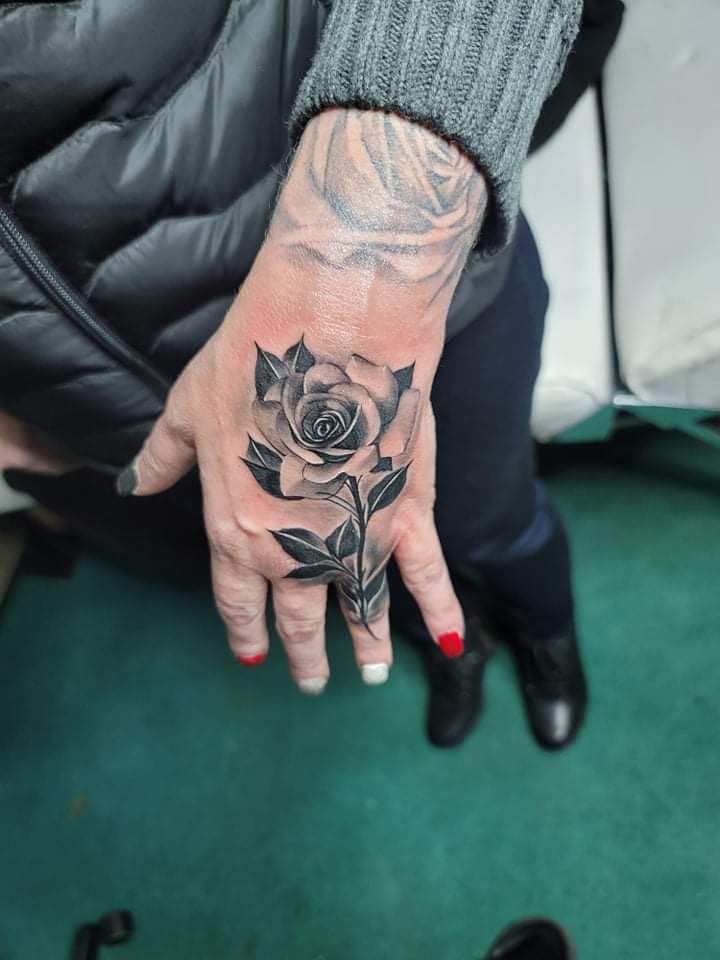 Hand with a detailed black and gray rose tattoo, nail polish, and a visible sleeve.