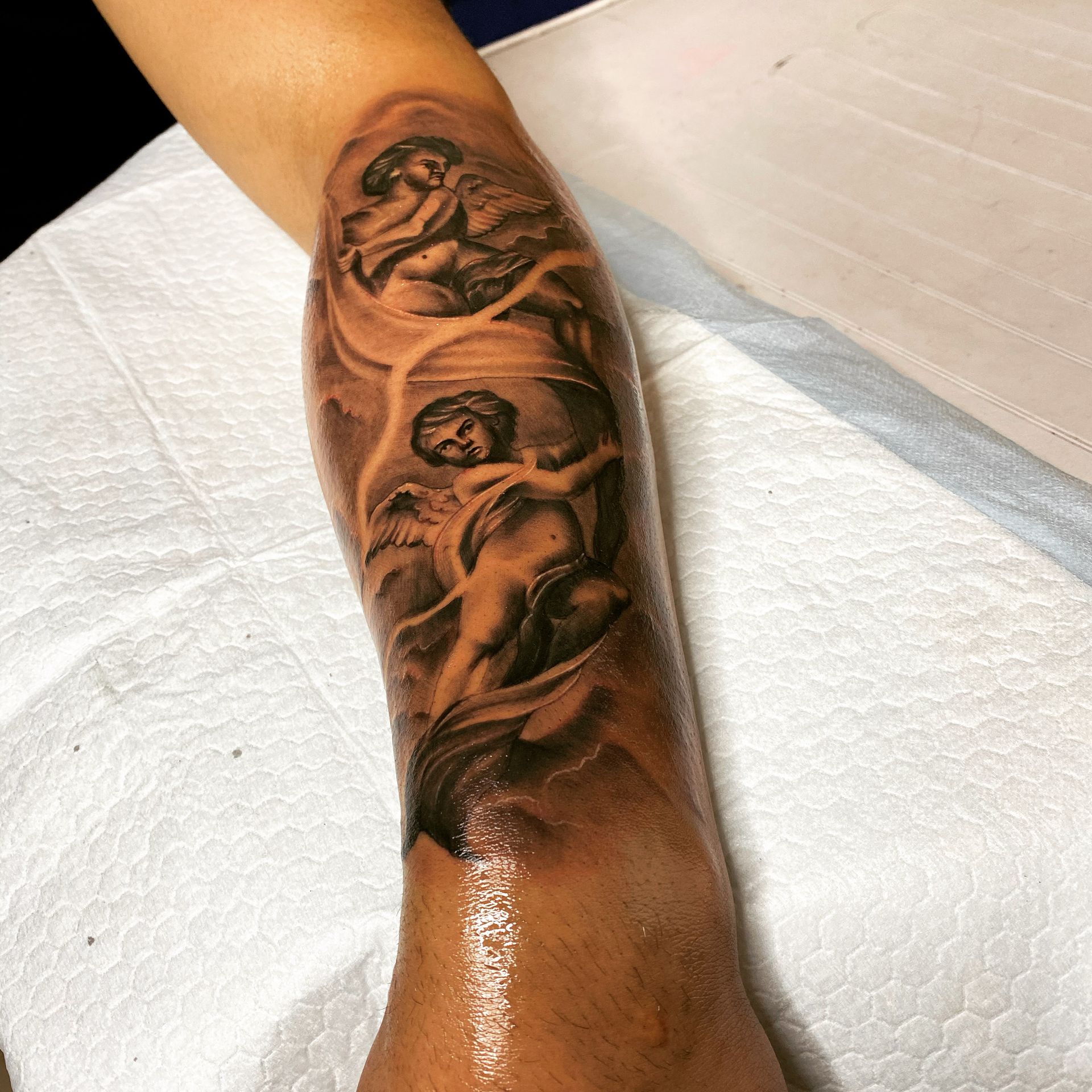 Tattoo of cherubs in clouds on an arm, with a grayscale shading.