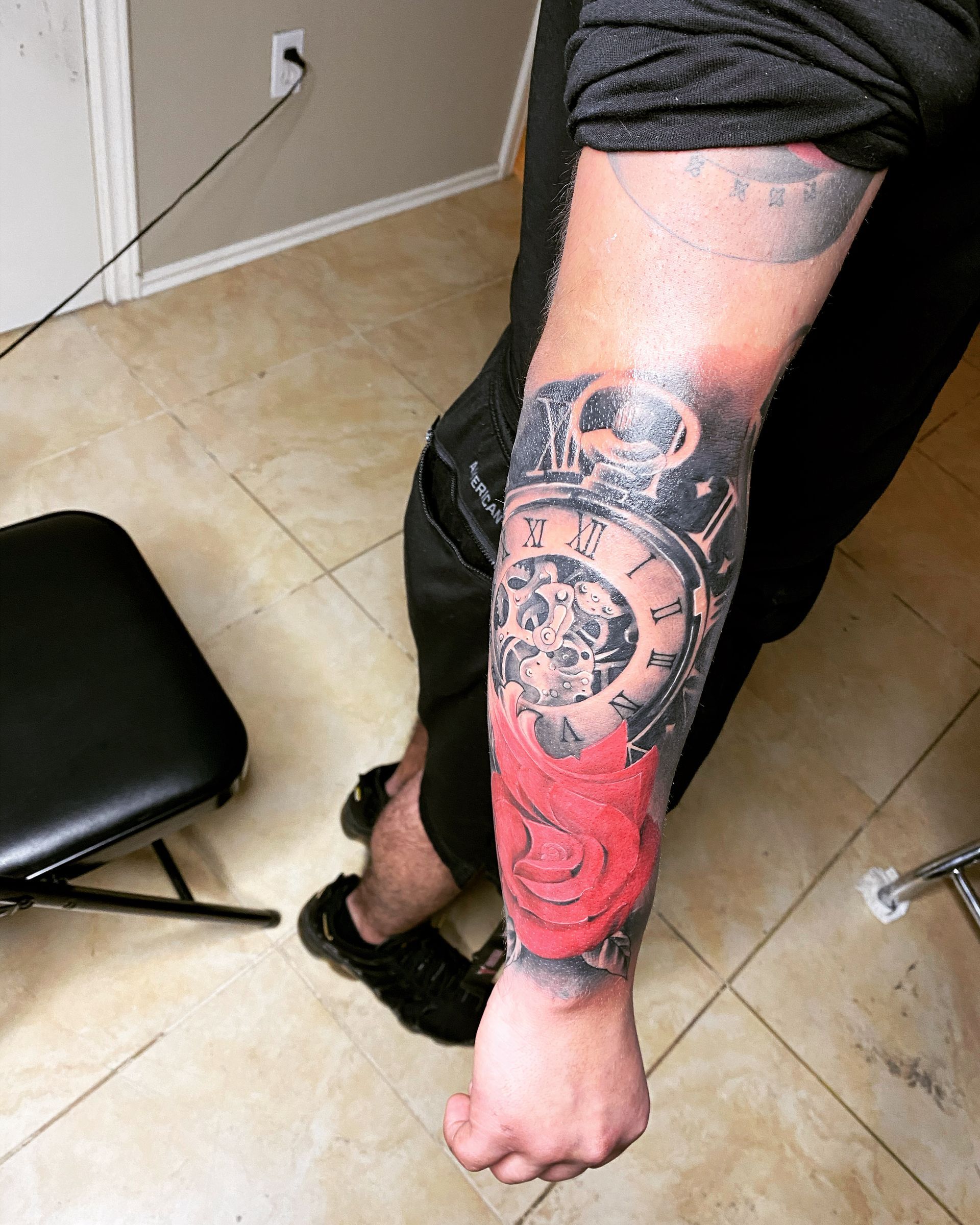 Tattoo of a pocket watch with a red rose on a person's forearm.