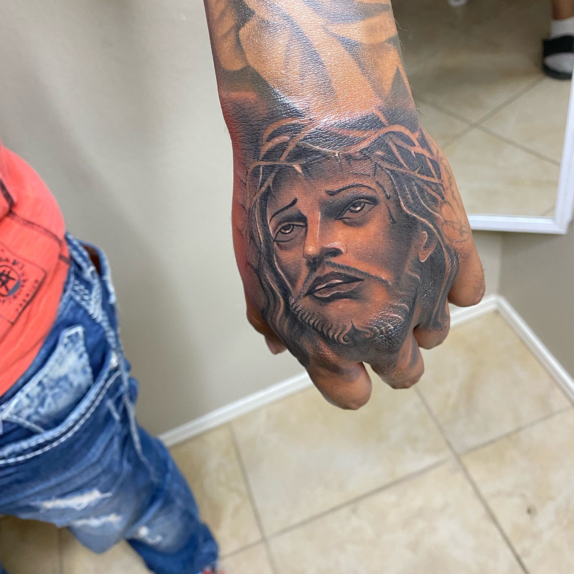 Hand tattoo of Jesus with a crown of thorns; dark skin tone.