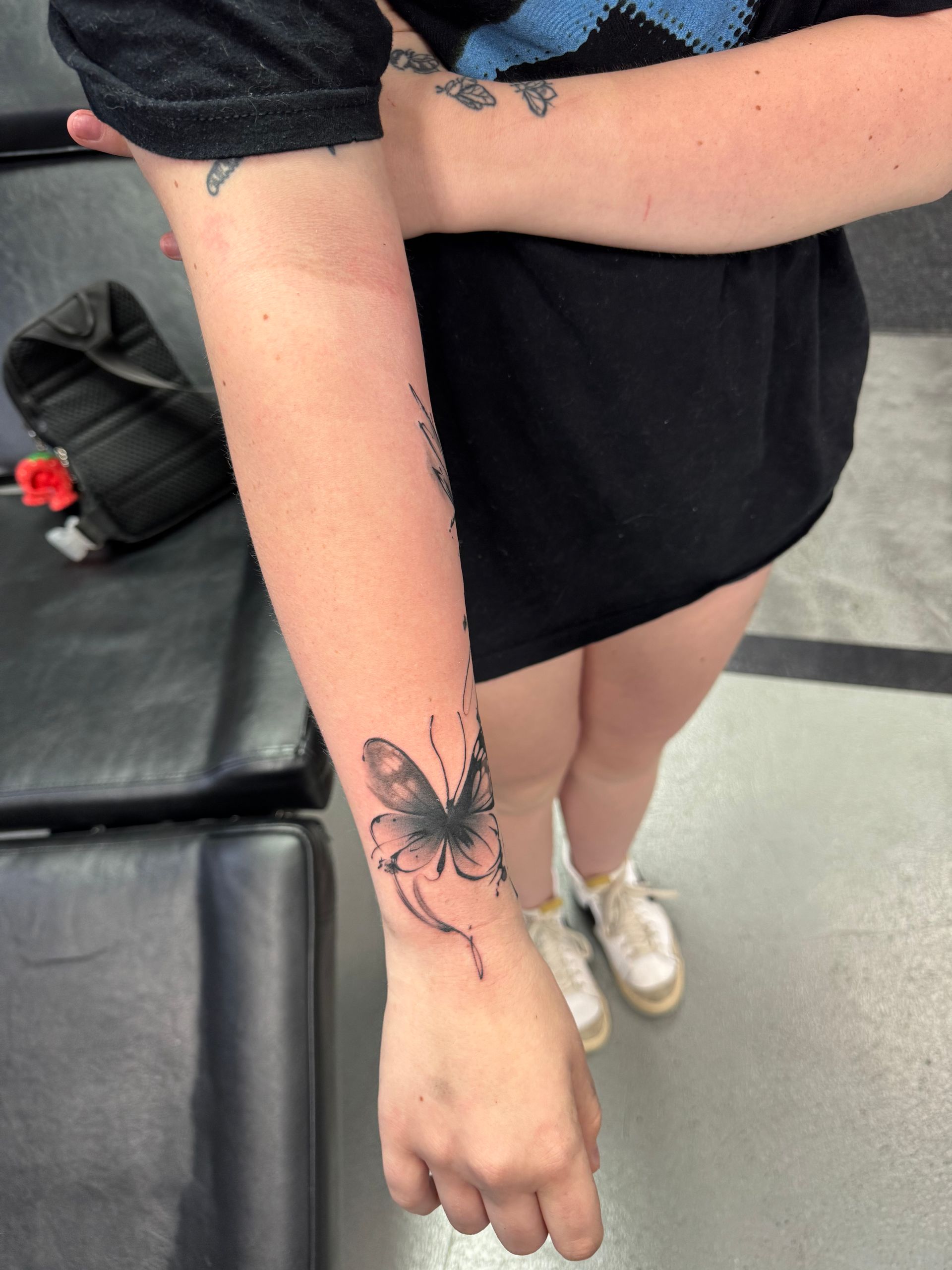 Person with forearm tattoo of a butterfly, in a tattoo shop.