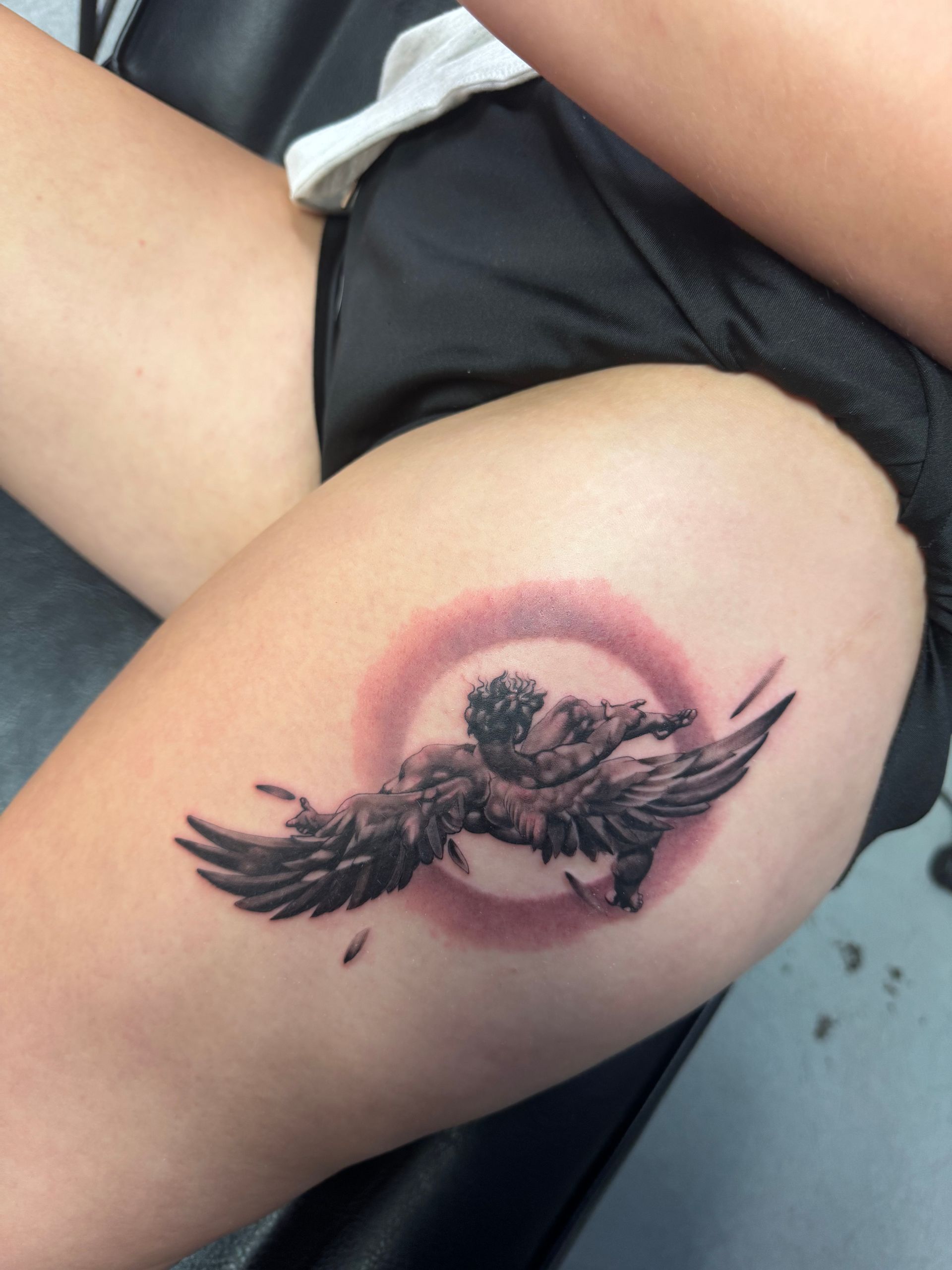 Tattoo of a flying bird with a smaller bird on its back, set in a red circle on a thigh.