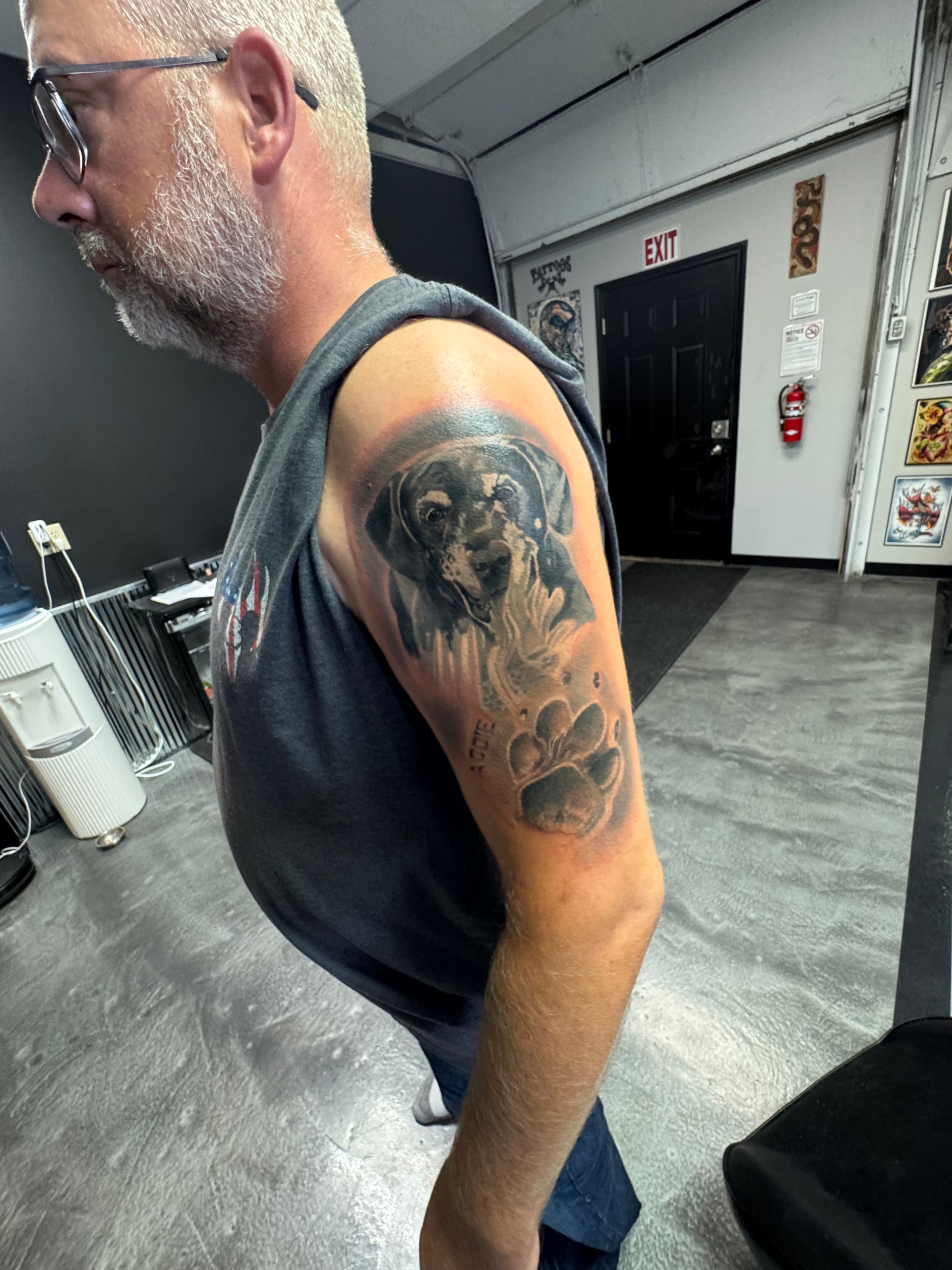 Man with gray beard and arm tattoo of a dog, indoors. Tattoo includes paw prints.