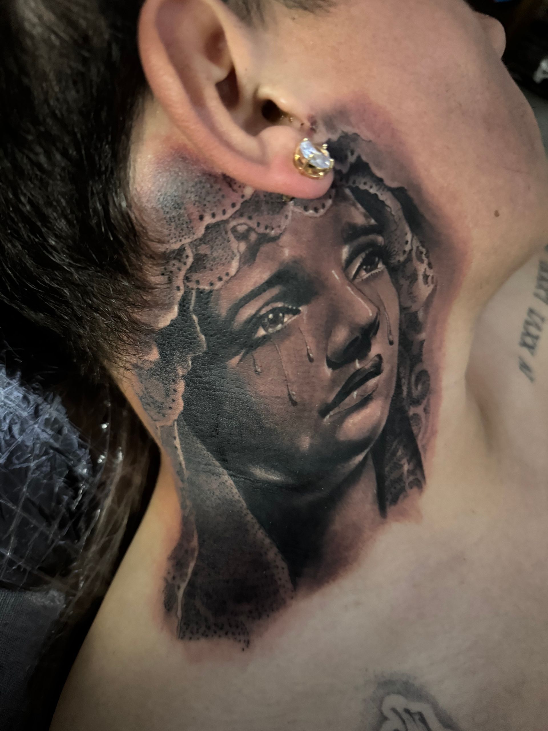 Black and grey tattoo of a sorrowful woman's face, tears falling, on a person's neck.