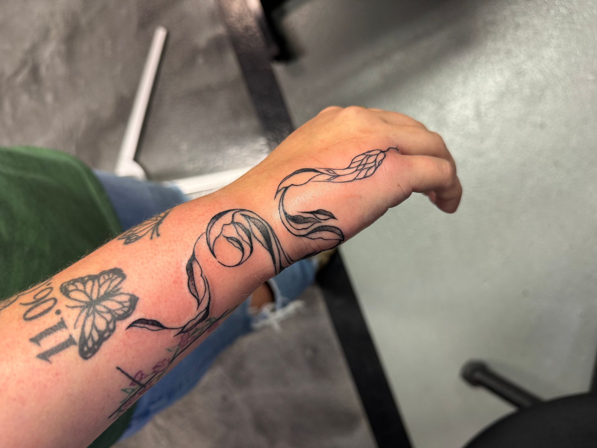 Person's arm with snake tattoo wrapping from wrist to hand. Butterfly tattoo and other art visible.