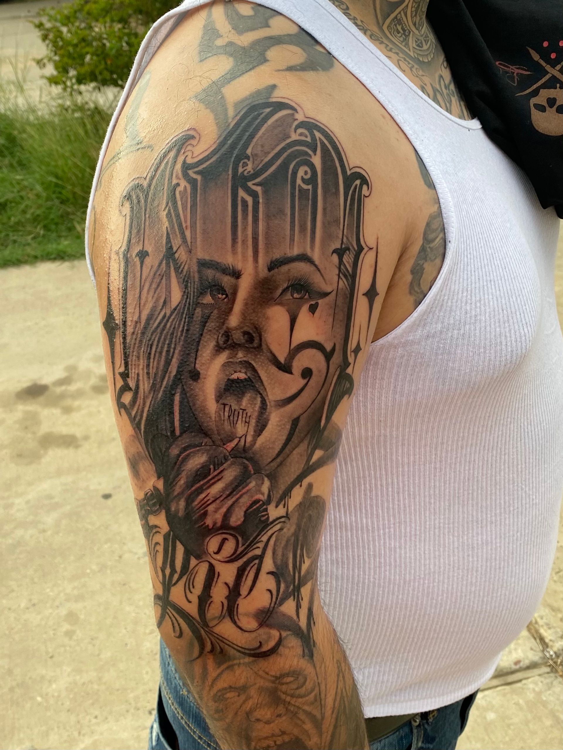 Man's arm with detailed black and gray tattoo: female face with open mouth, ornate design, and