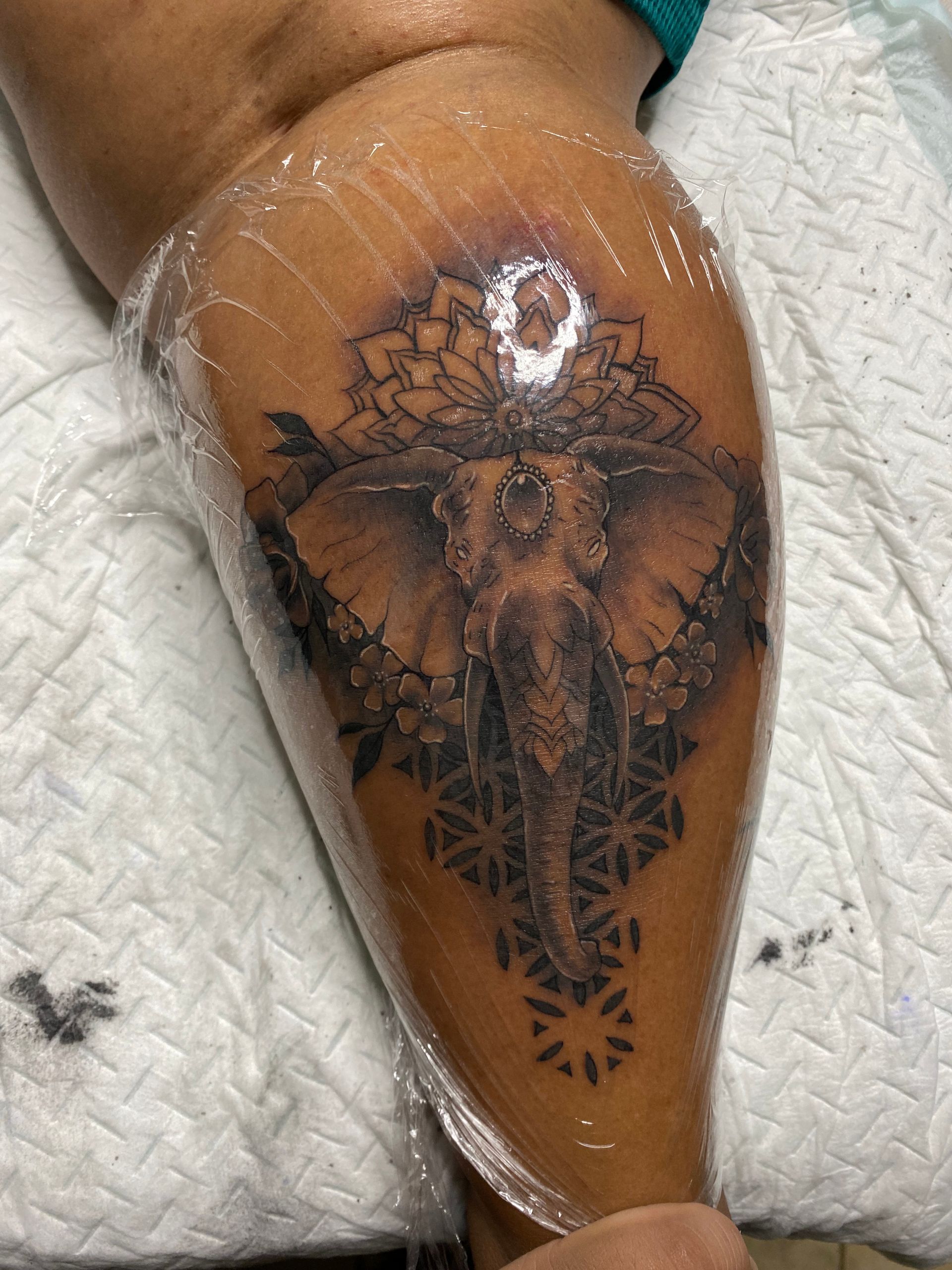 Tattoo of an elephant with a geometric design on a person's leg, wrapped in plastic.