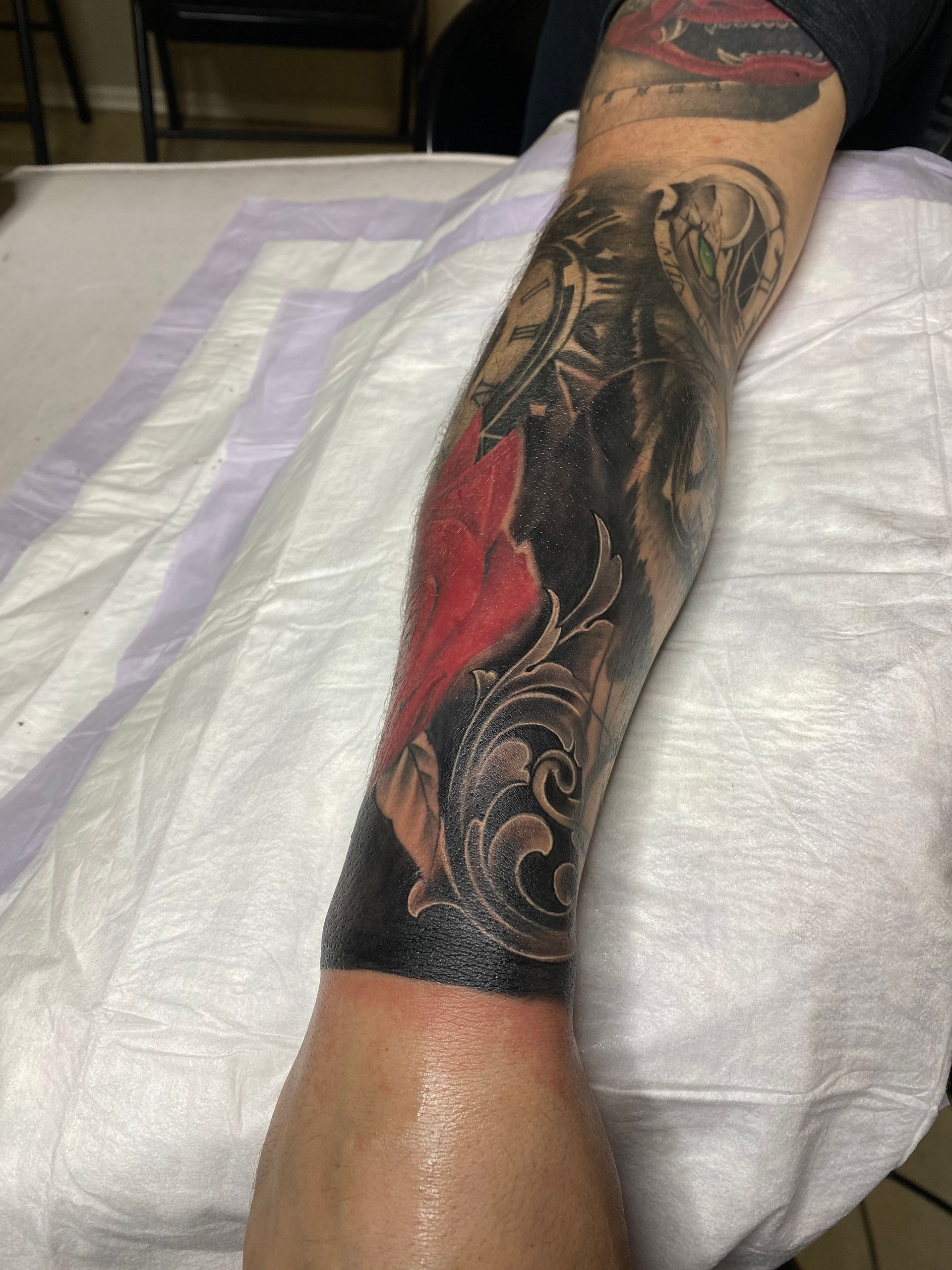 Arm tattoo with red heart, black shading, and detailed scrollwork on a white surface.