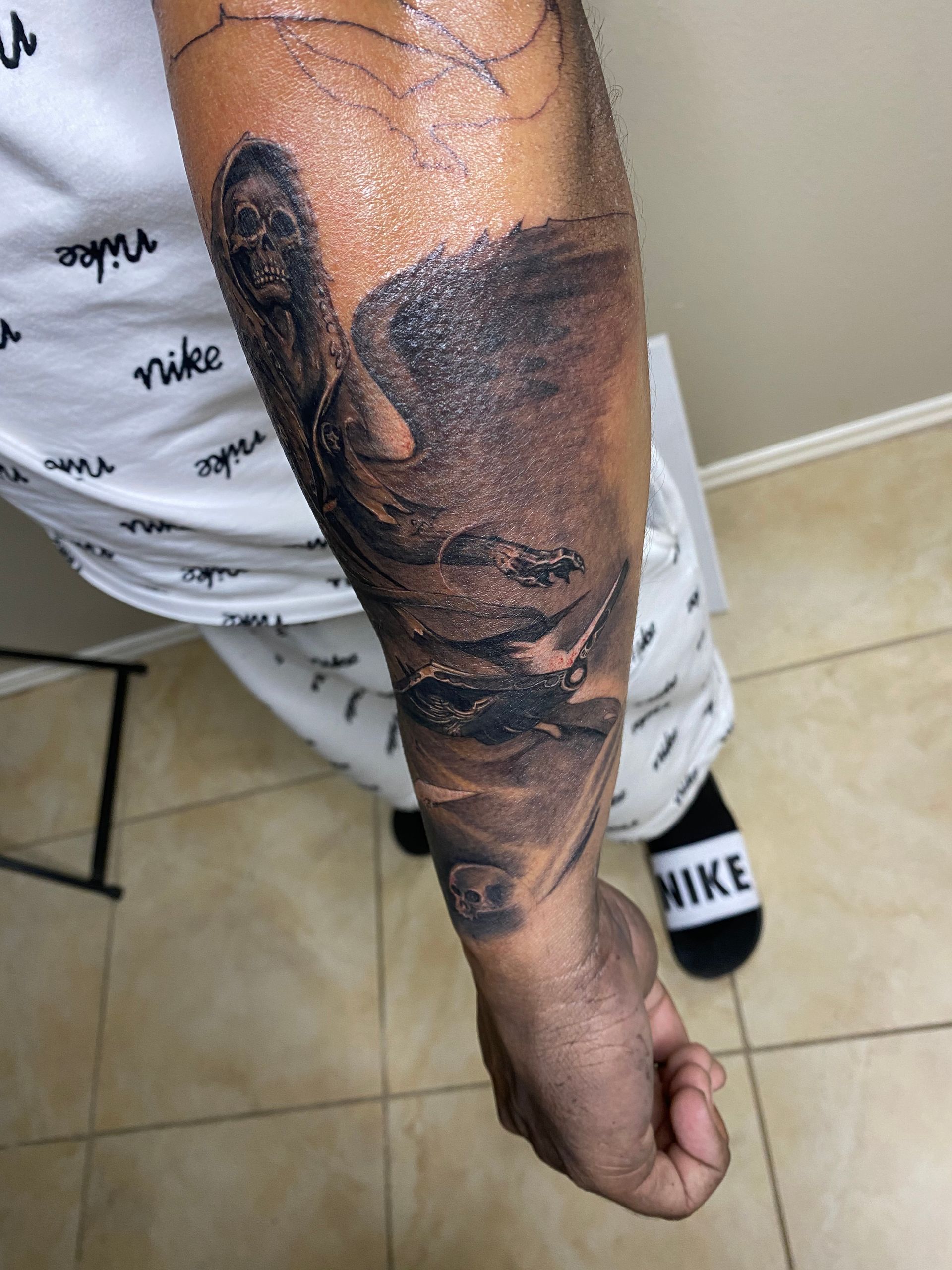 Person's arm with dark ink tattoo depicting a swirling, shadowy scene; wearing white Nike shirt and sweatpants.